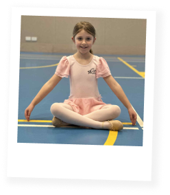Girl wearing a pink ballet dress sitting cross legged on the floor with arms in demi bra and smiling