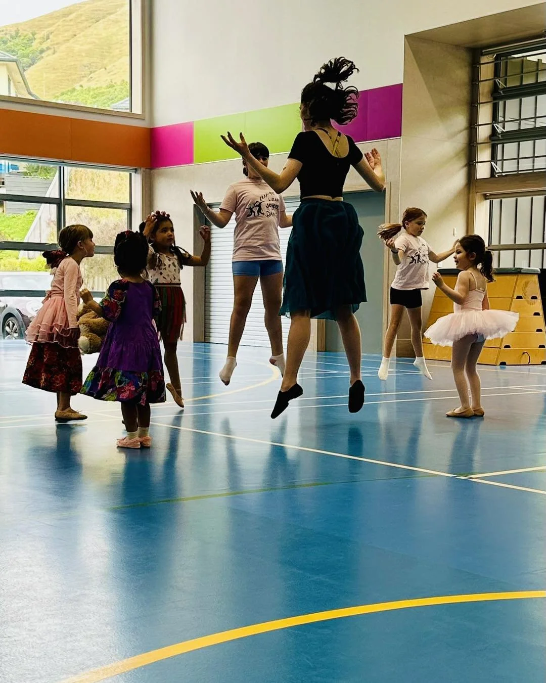 Dance class with children jumping in gymnasium.
