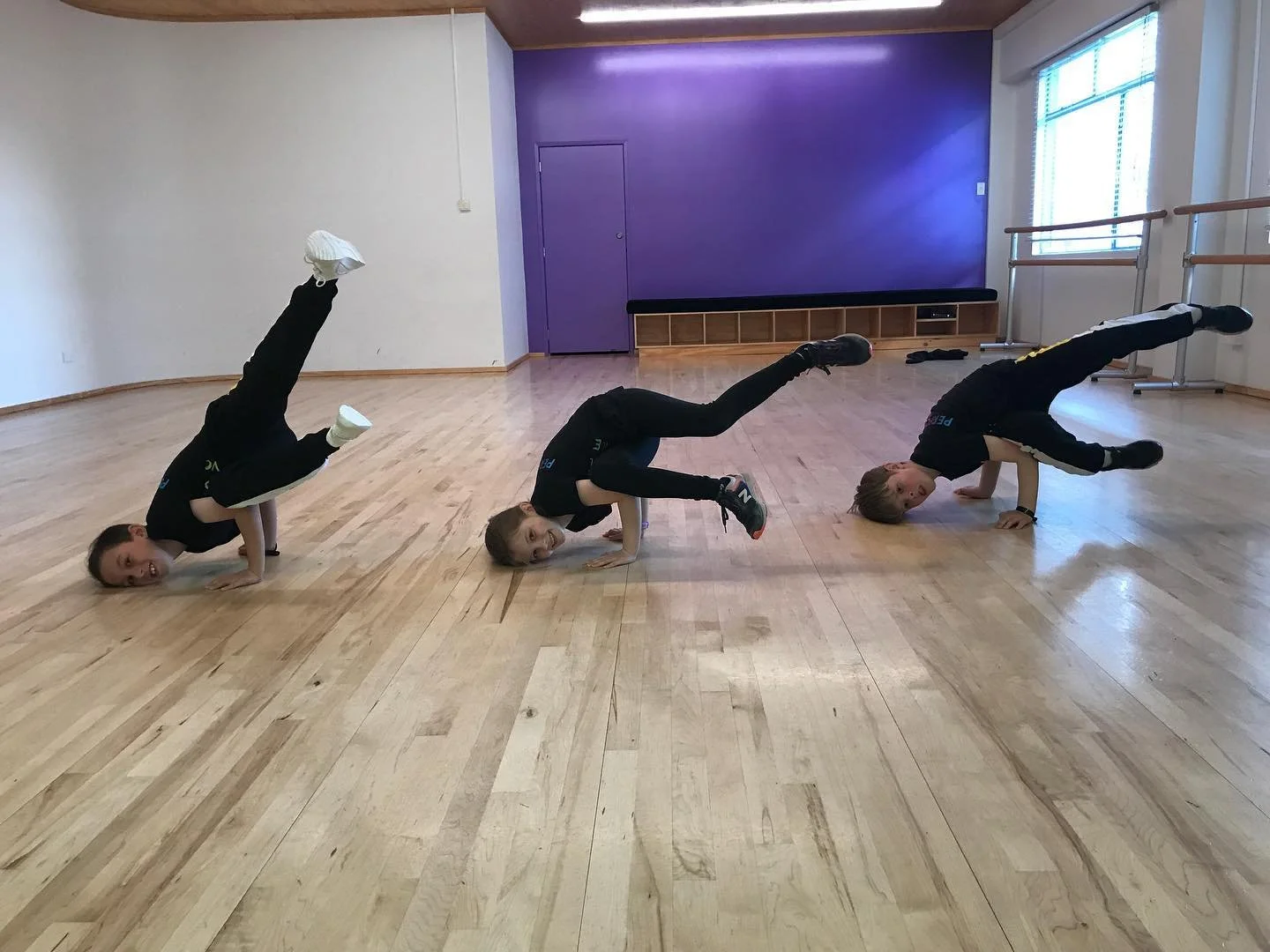 Three kids doing hip hop shoulder stands in a dance studio