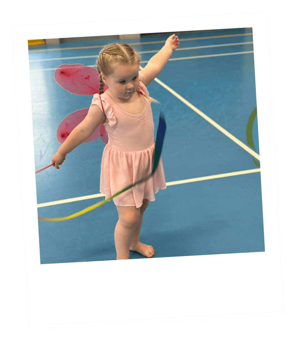 Young girl dressed as a fairy practicing with a hula hoop in a gymnasium.