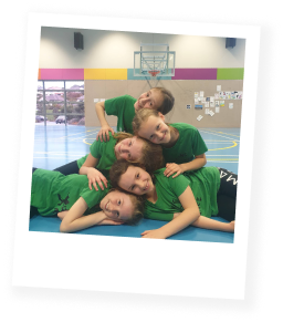 A group of five children in green t-shirts, posing in gymnasium-based dance studio