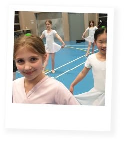 Group of young girls in white ballet dresses practicing ballet in a dance studio with blue flooring