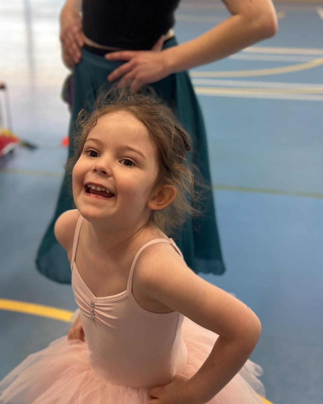 Young girl in a ballet costume smiling with hands on hips in a gymnasium.