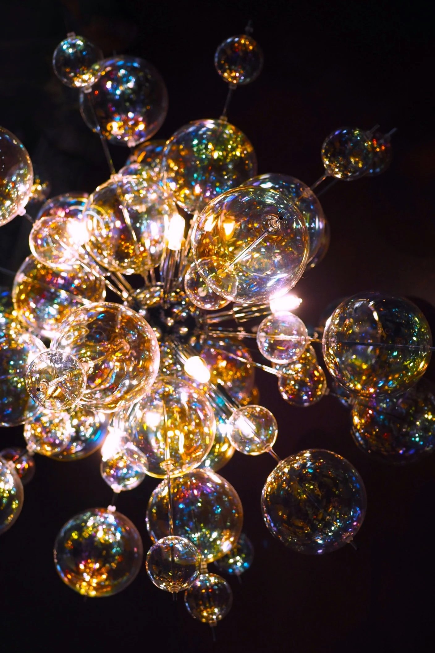 A chandelier with numerous glass globes that reflect colorful lights against a dark background.