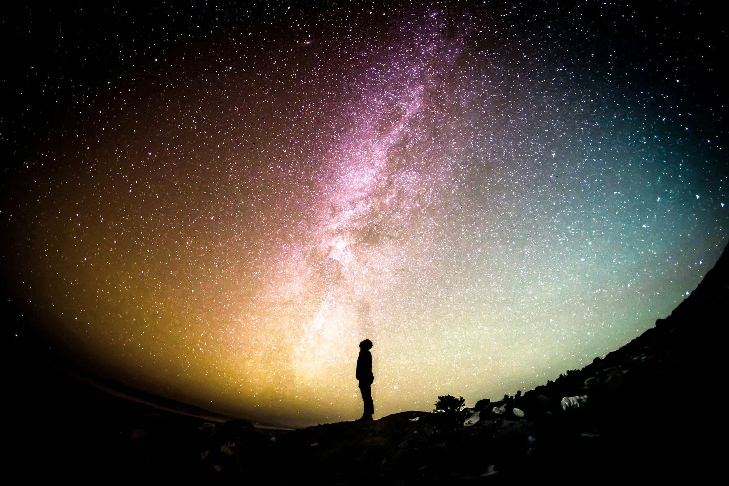 Person standing outdoors at night near a star-filled sky and the Milky Way galaxy.