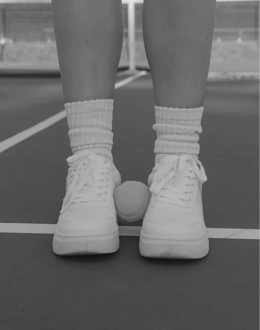 Tennis ball between white sneakers on tennis or pickleball court