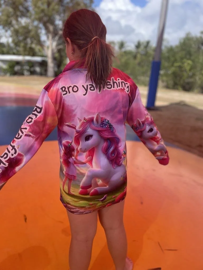 Child in a pink unicorn-themed raincoat on an orange trampoline.