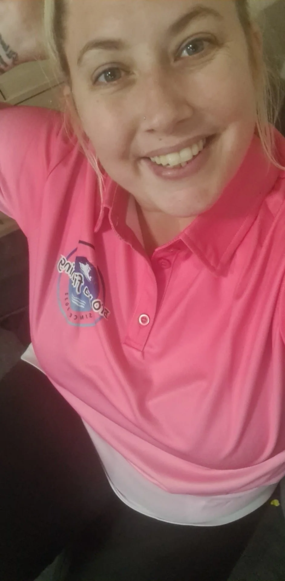 A woman smiling, wearing a pink uniform with a logo on the chest, looking up at the camera.