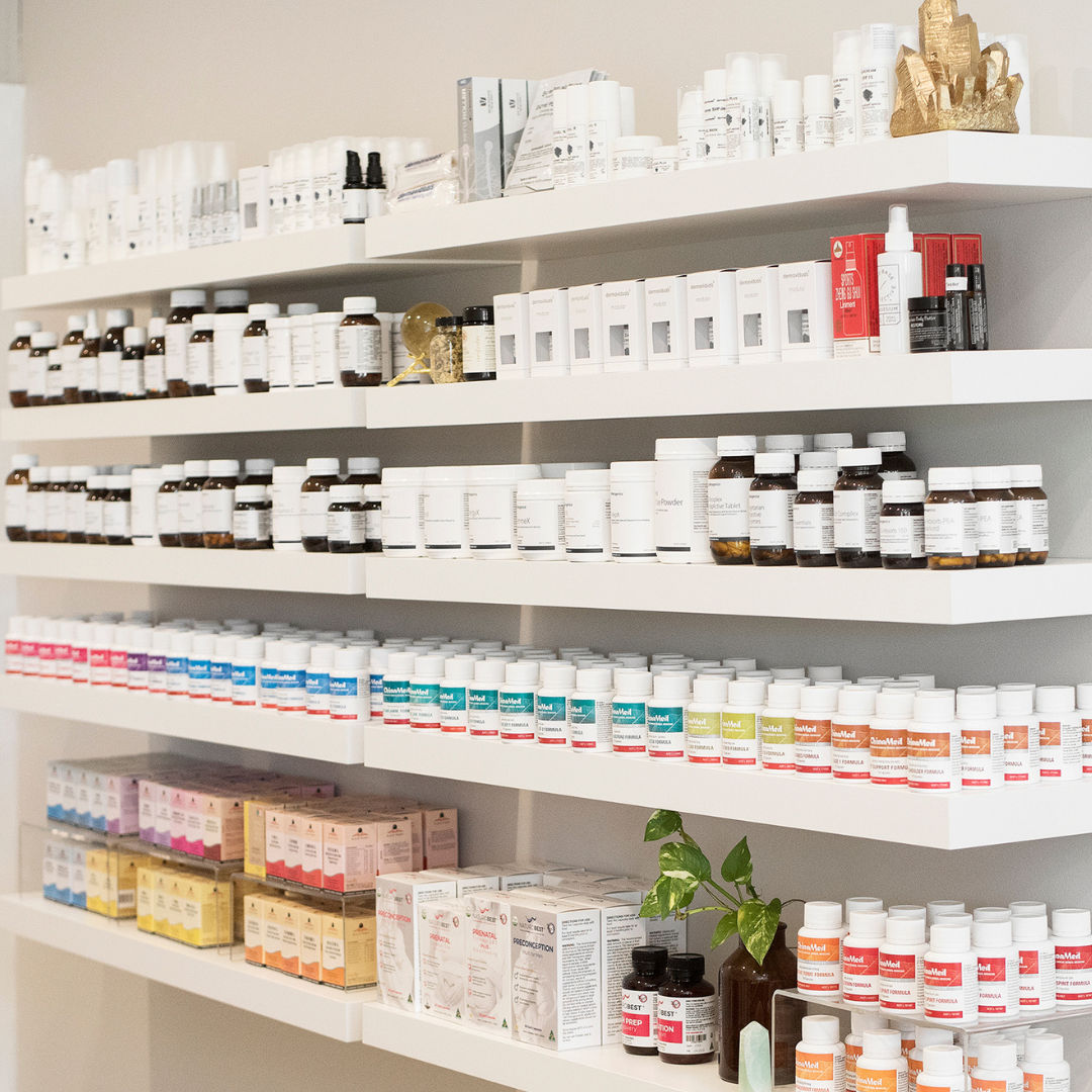 A clear glass bowl on a wooden surface contains pink and white objects, with paper game pieces inside, some with the word 'JOY.' The background is blurred greenery.