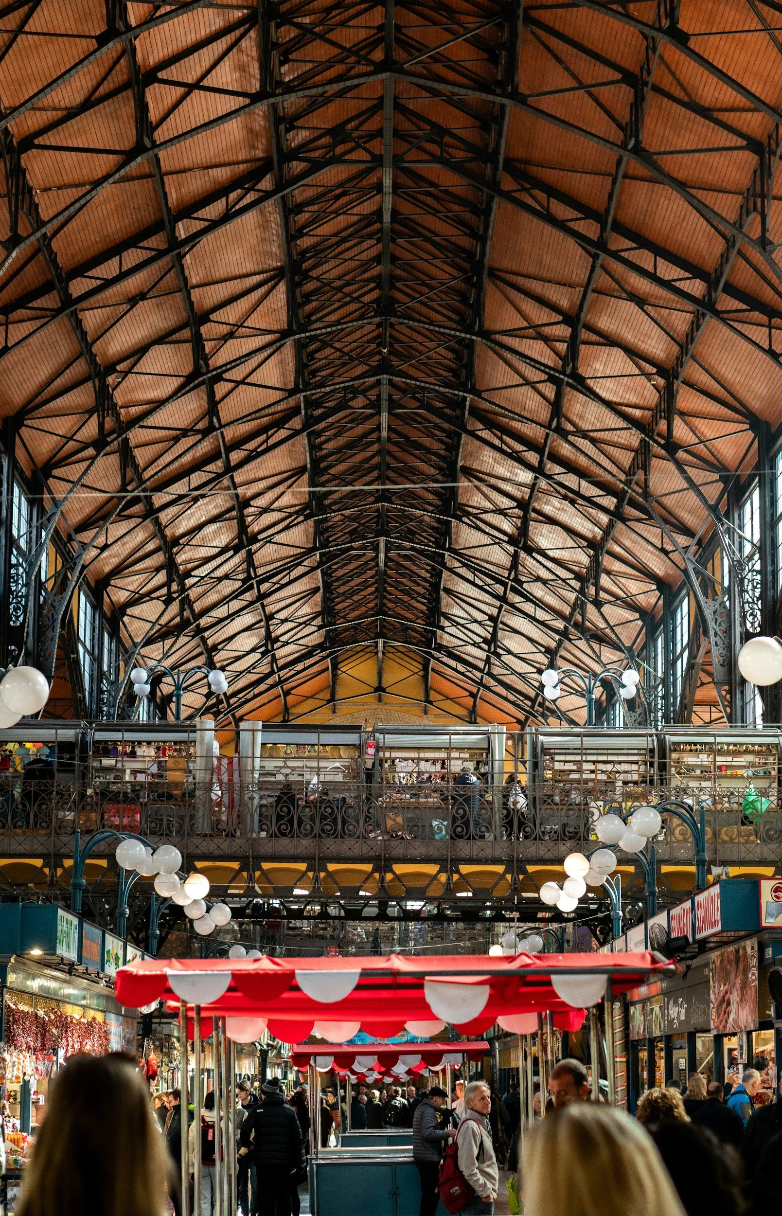 Interior of the bustling Riverside Market with a high arched ceiling made of wood and metal beams, lined with shops and vendors, and people walking underneath.
