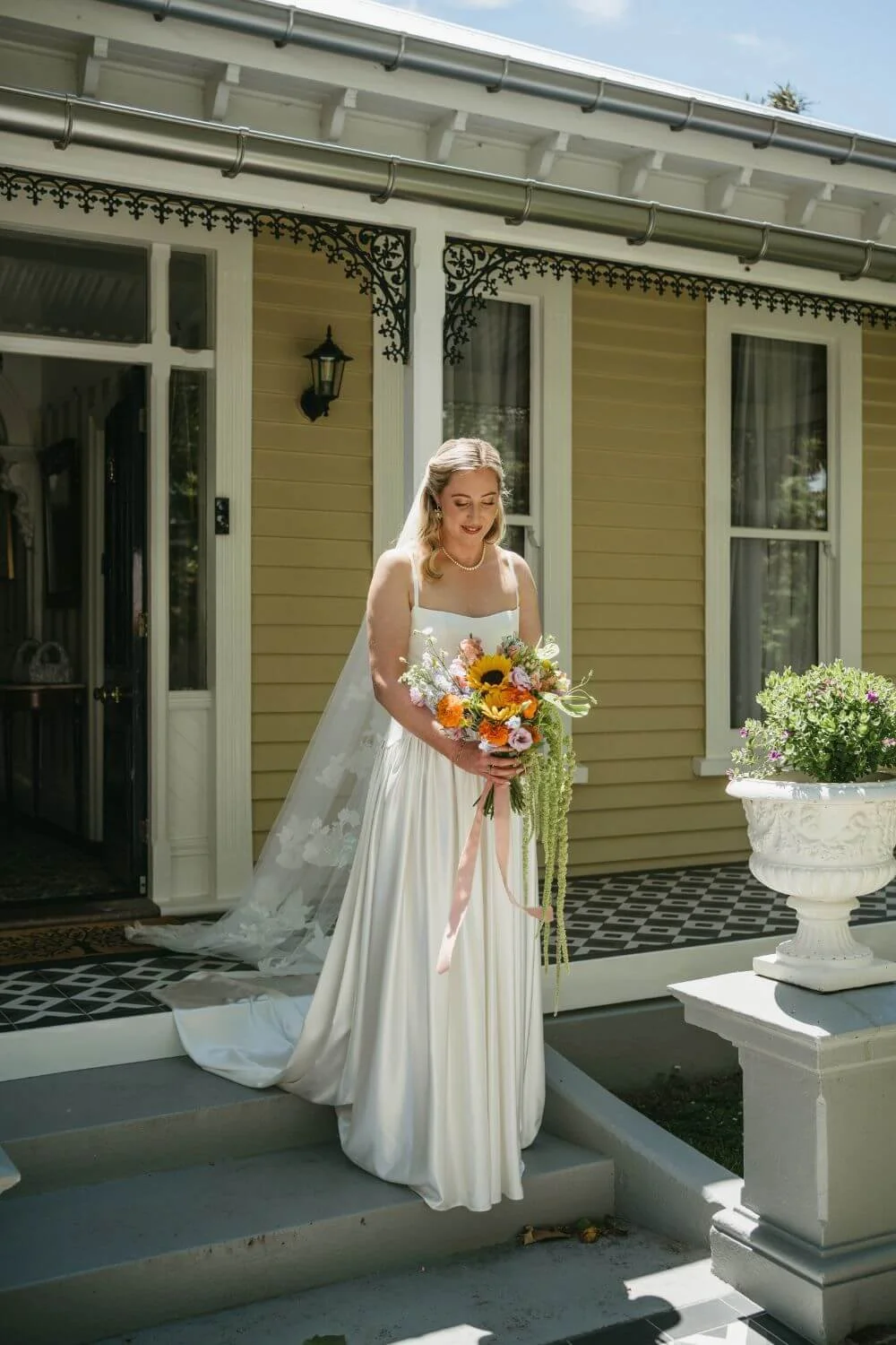 Bride walking out of [plane tree villa with flower bouquet.