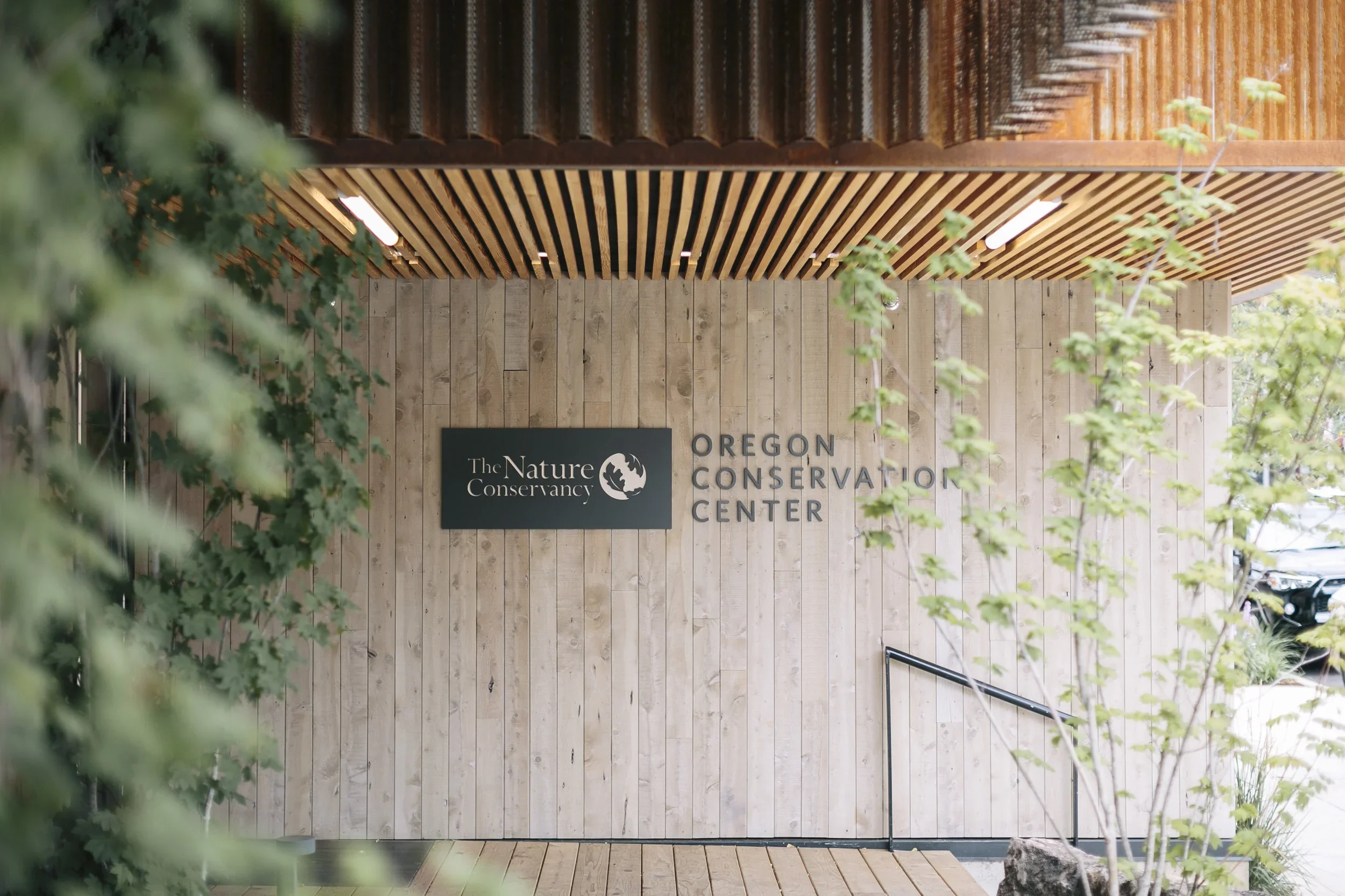 Entrance sign for the Oregon Conservation Center at The Nature Conservancy, mounted on a wood-paneled wall with greenery in the foreground.