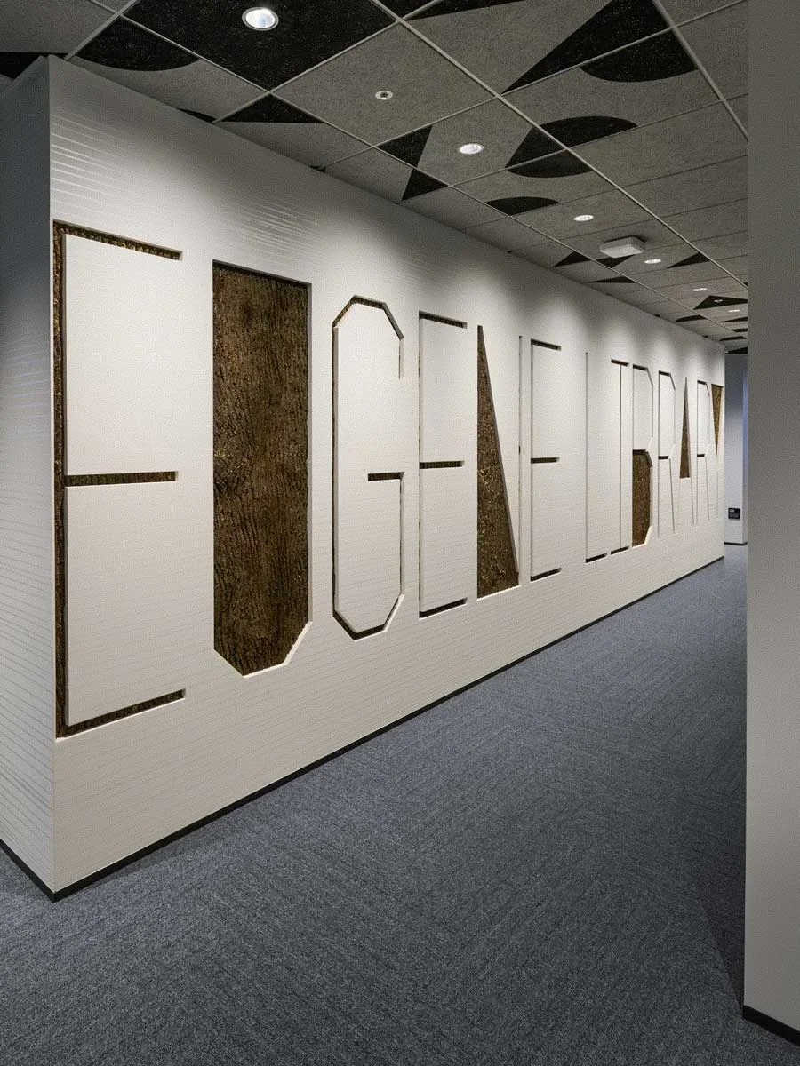 Wall with large cut-out letters spelling 'COLLABORATE' in a modern office hallway.