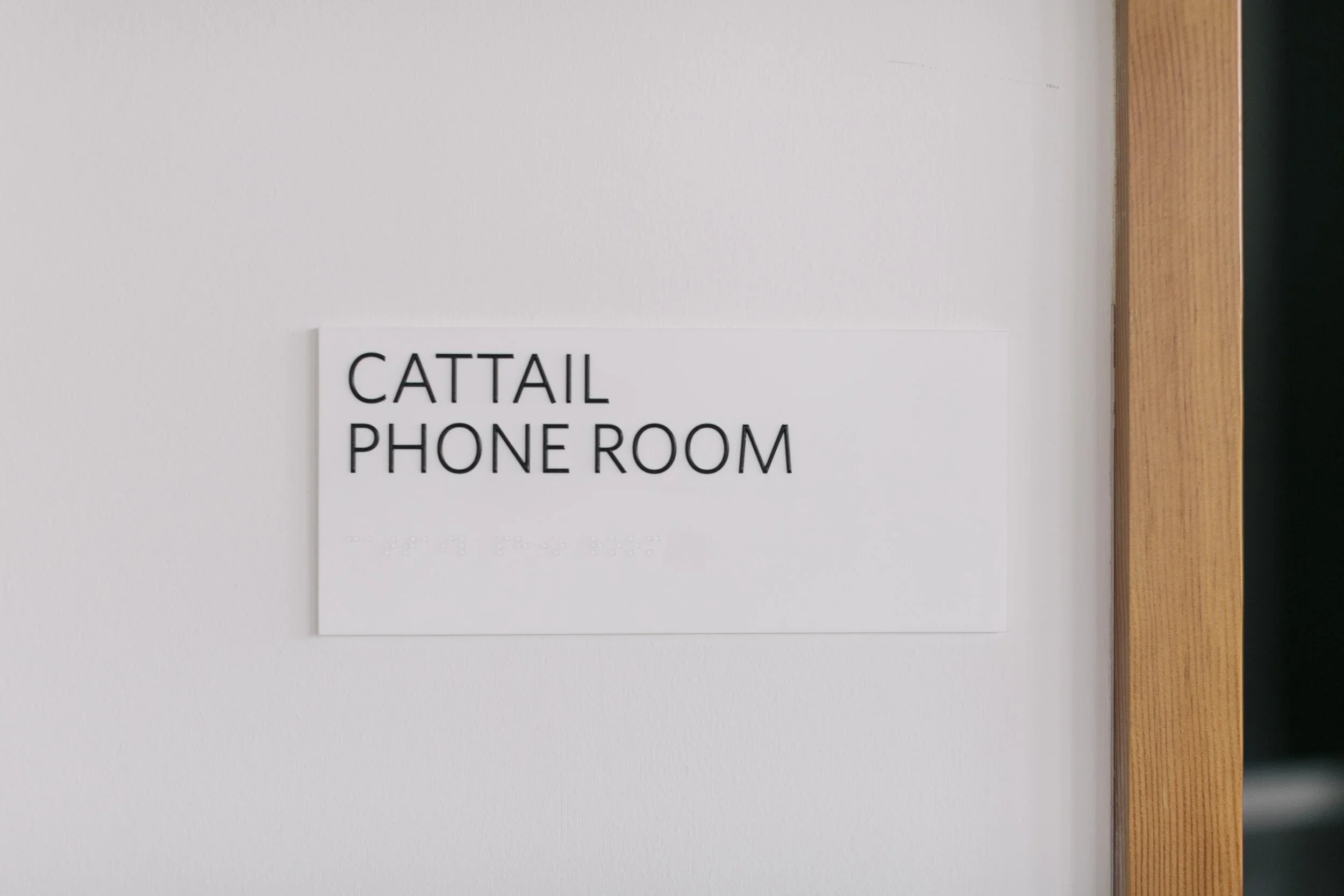 Sign on a white wall reading 'CATTail Phone Room' with a wooden door frame on the right.