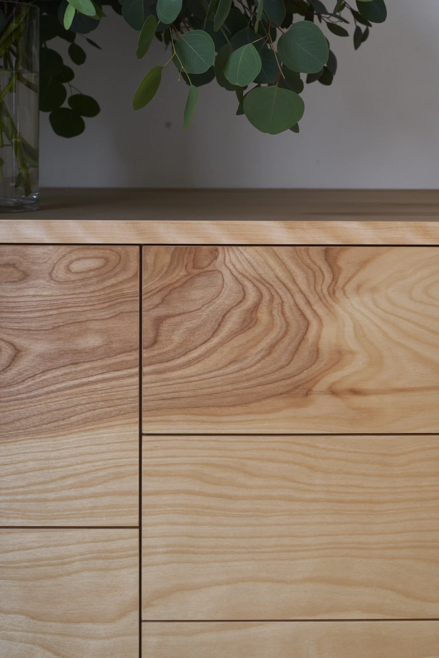 Close-up of a wooden cabinet with visible grain patterns and a green leafy plant on top.