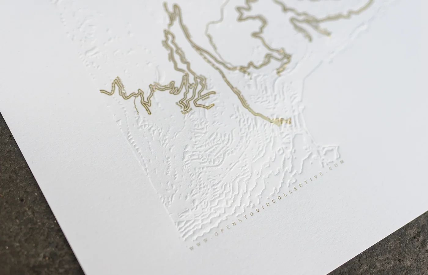 Close-up of a textured map of North America with raised borders on white paper, featuring gold accents and the website URL 'WWW.OPENSTUDIOCOLLECTIVE.COM' at the bottom.