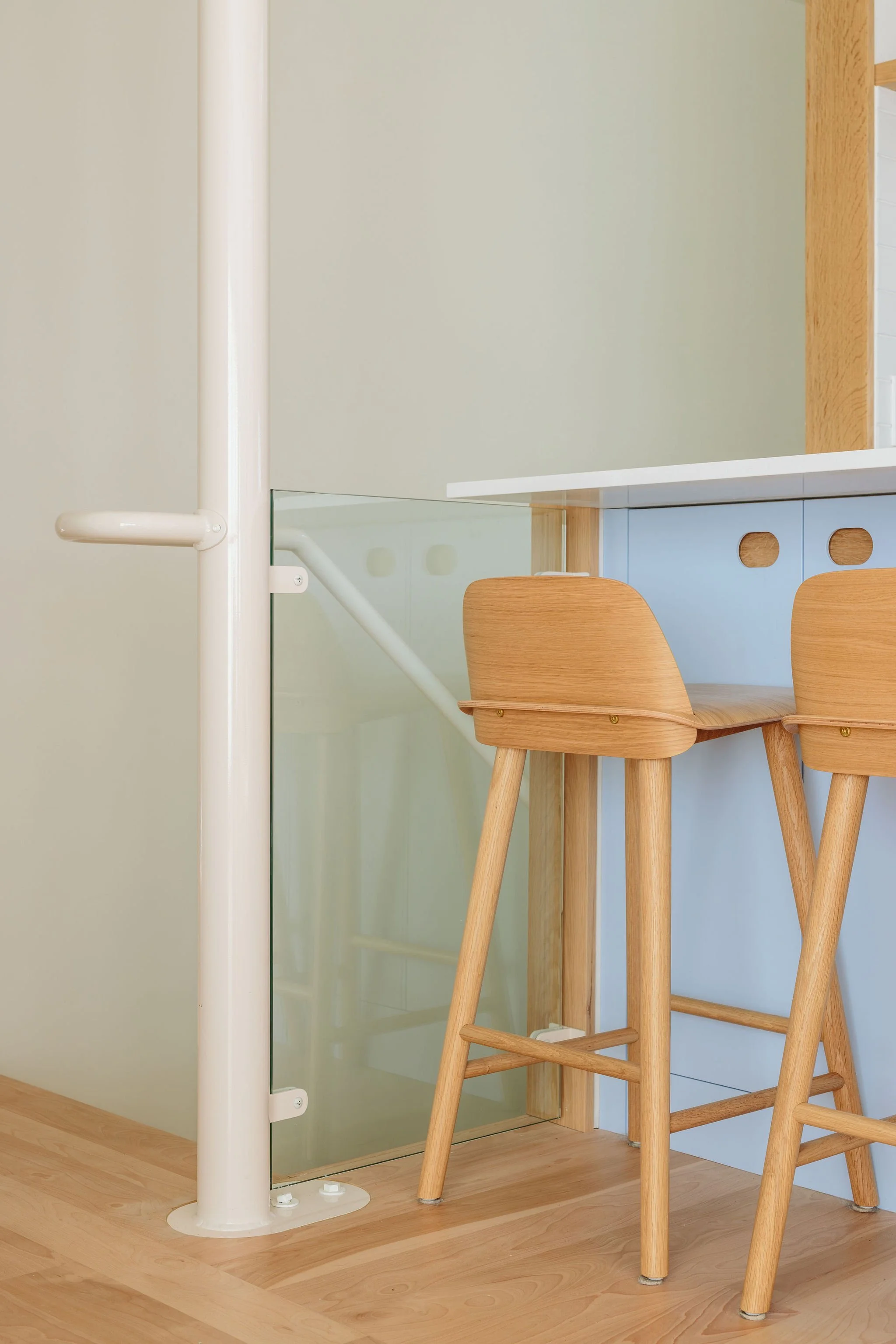 Close-up of wooden bar stools at a white counter in a modern kitchen with light wood flooring and beige walls.