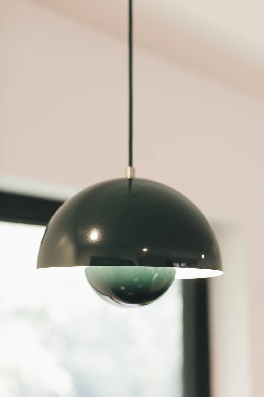 Modern black pendant light fixture hanging from the ceiling in a room with a blurred window in the background.