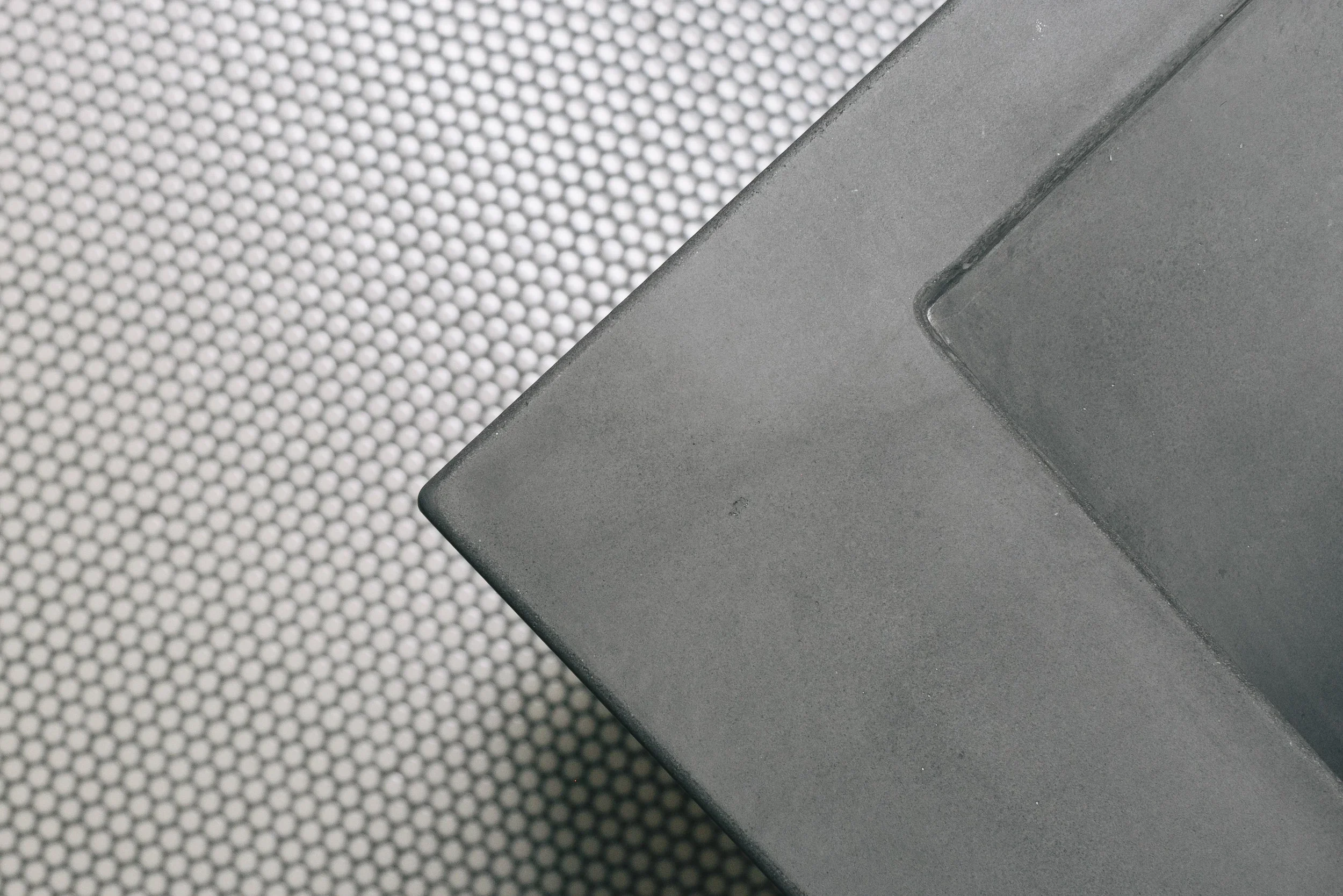 Close-up of a gray metal box or object on a textured surface with small circular patterns.