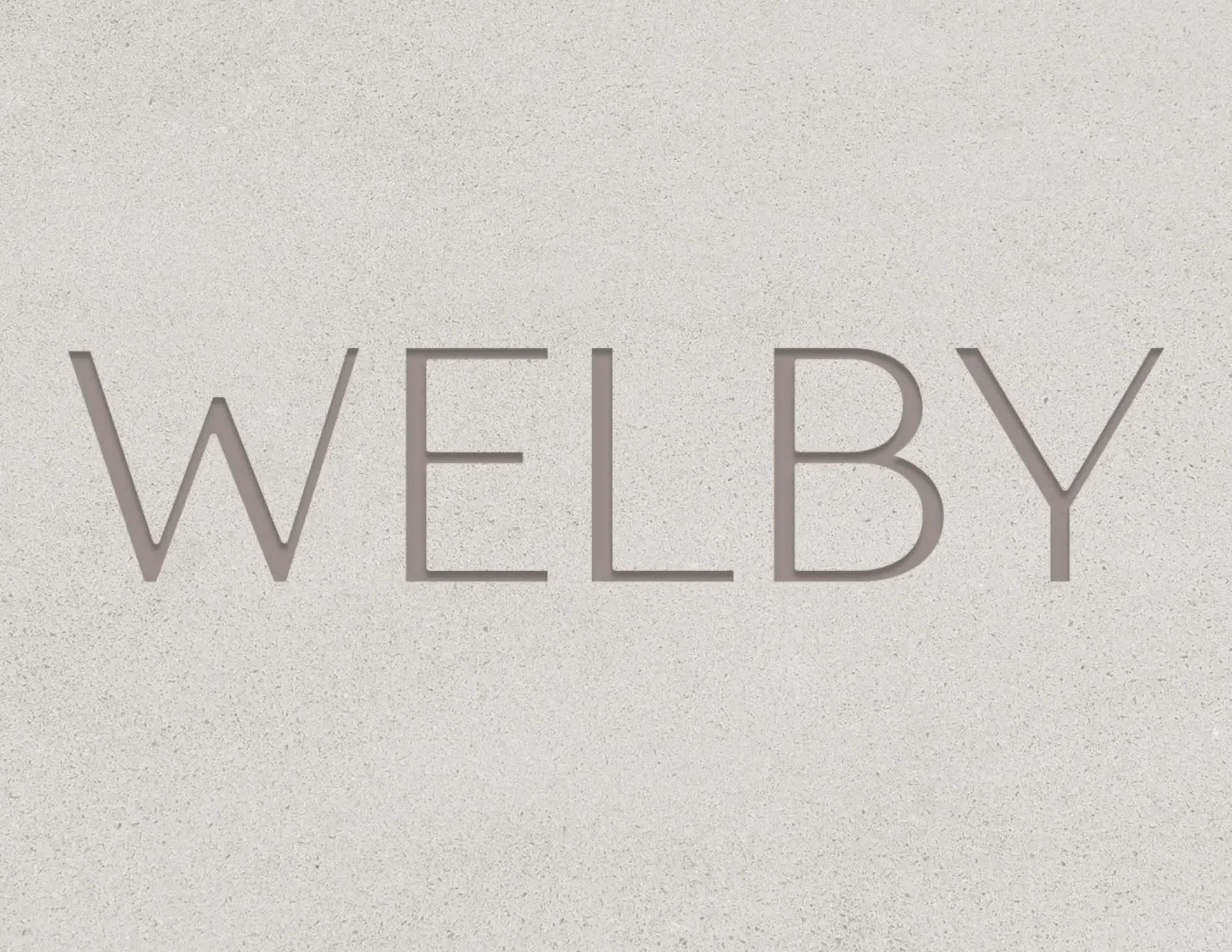 Close-up of a sign with the word 'WELBY' in large capital letters on a light-colored textured background.