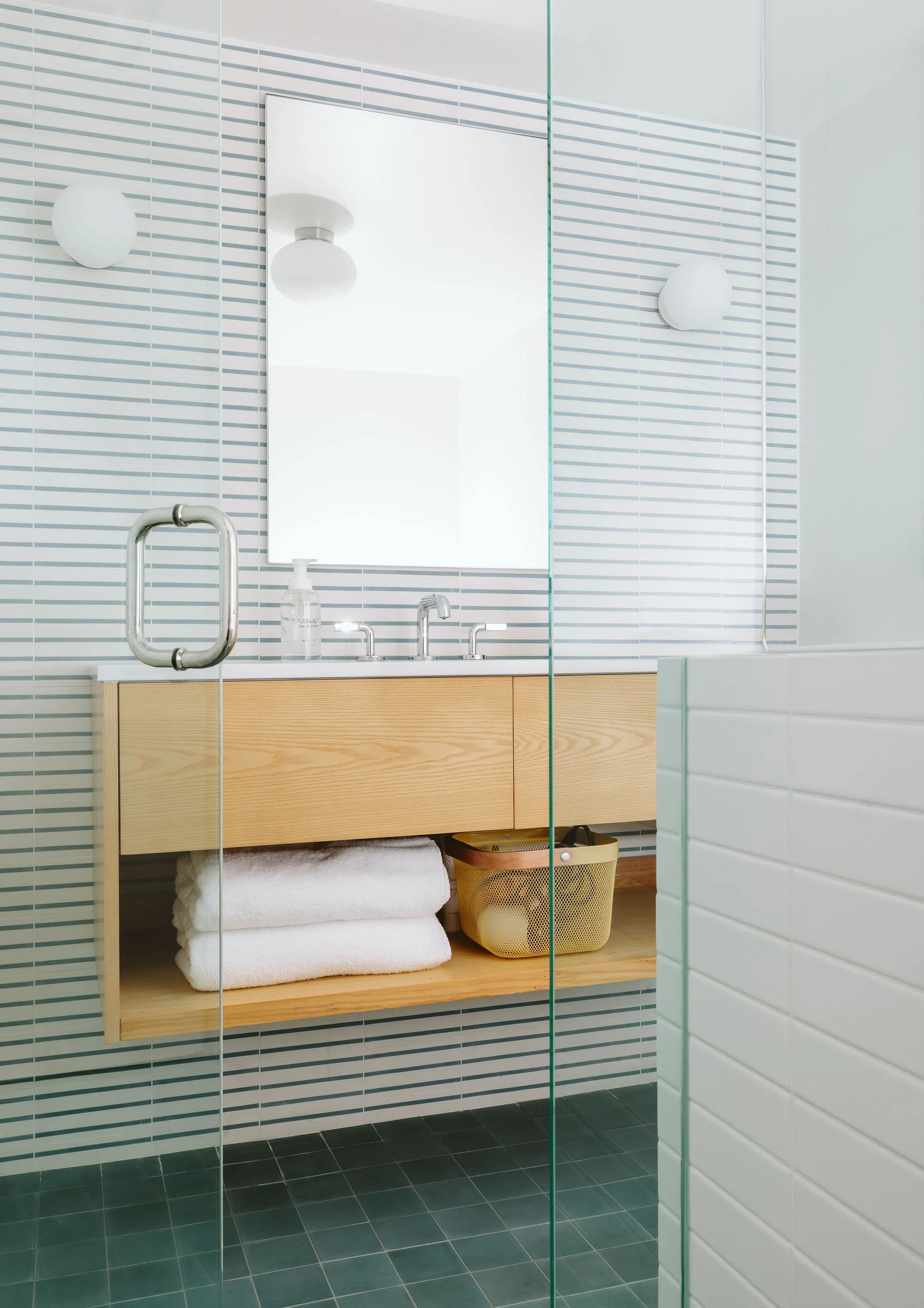 Clean modern bathroom with wooden vanity, folded towels, glass shower door, striped wall tiles, mirror, and ceiling lights.