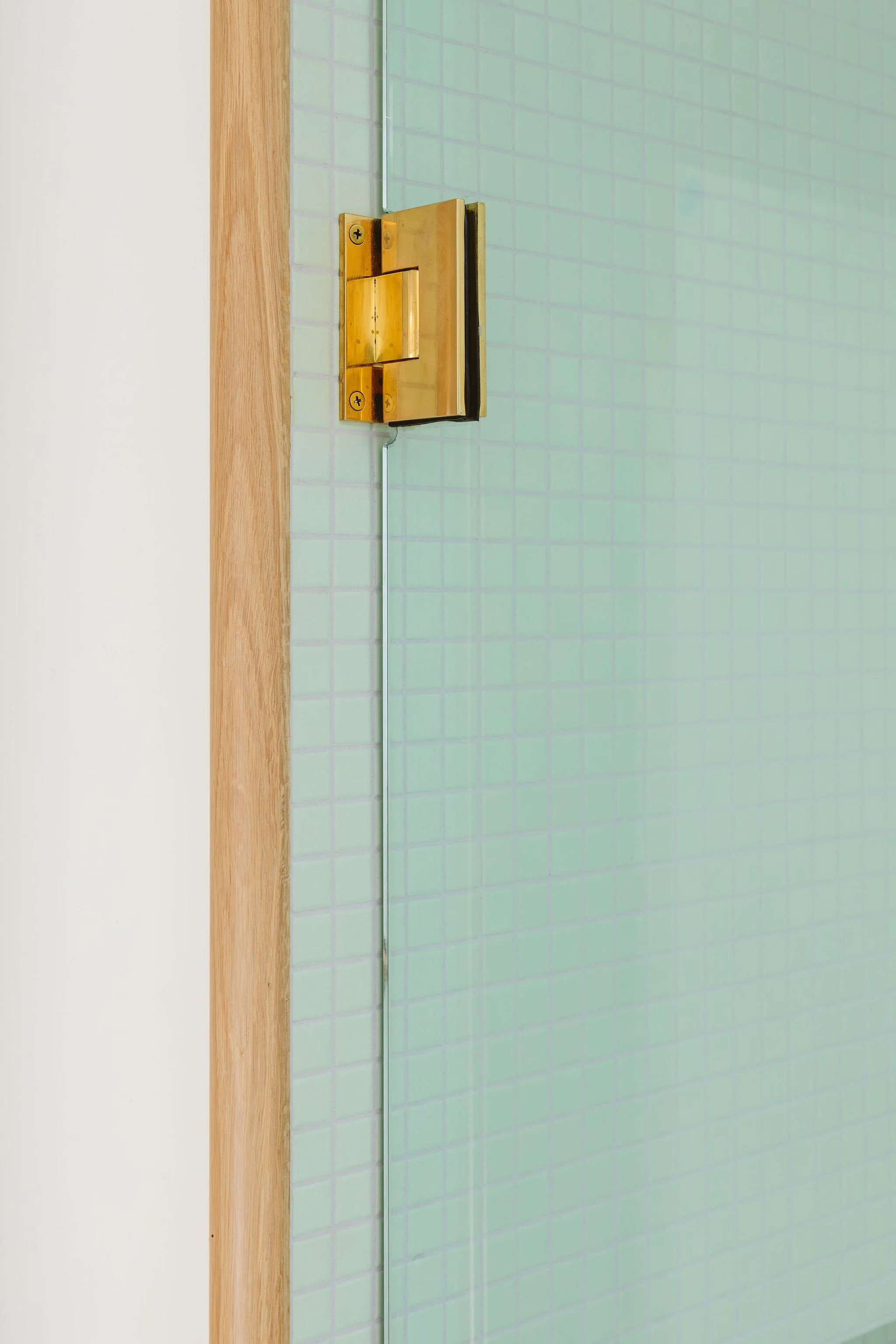 Close-up view of a door hinge on a green tiled wall with a wooden door frame.