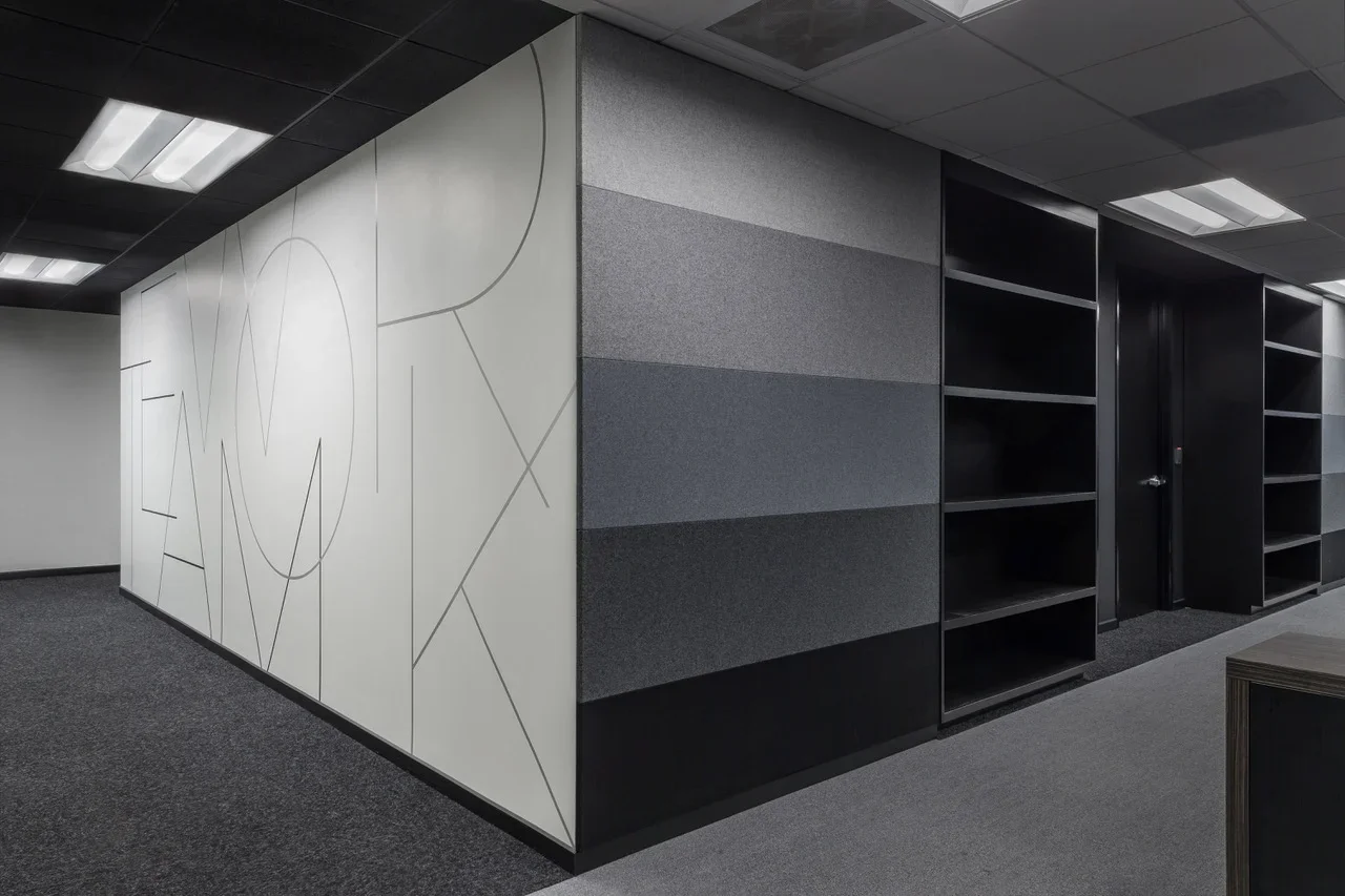Empty office space with black bookshelves, textured gray wall panels, and a large white wall with geometric line art.