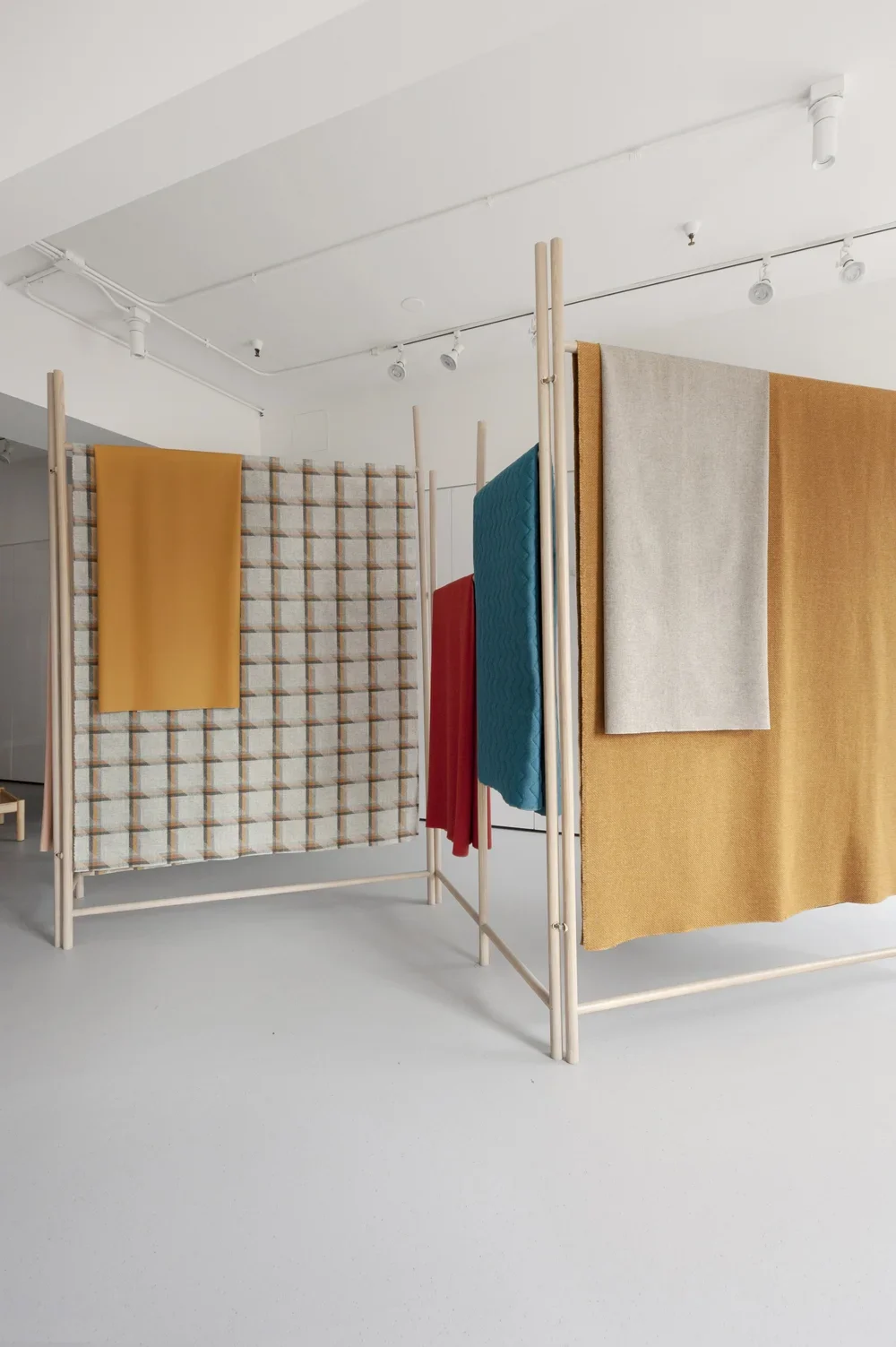 Display of colorful fabric swatches hanging on wooden frames in a minimalist gallery space.