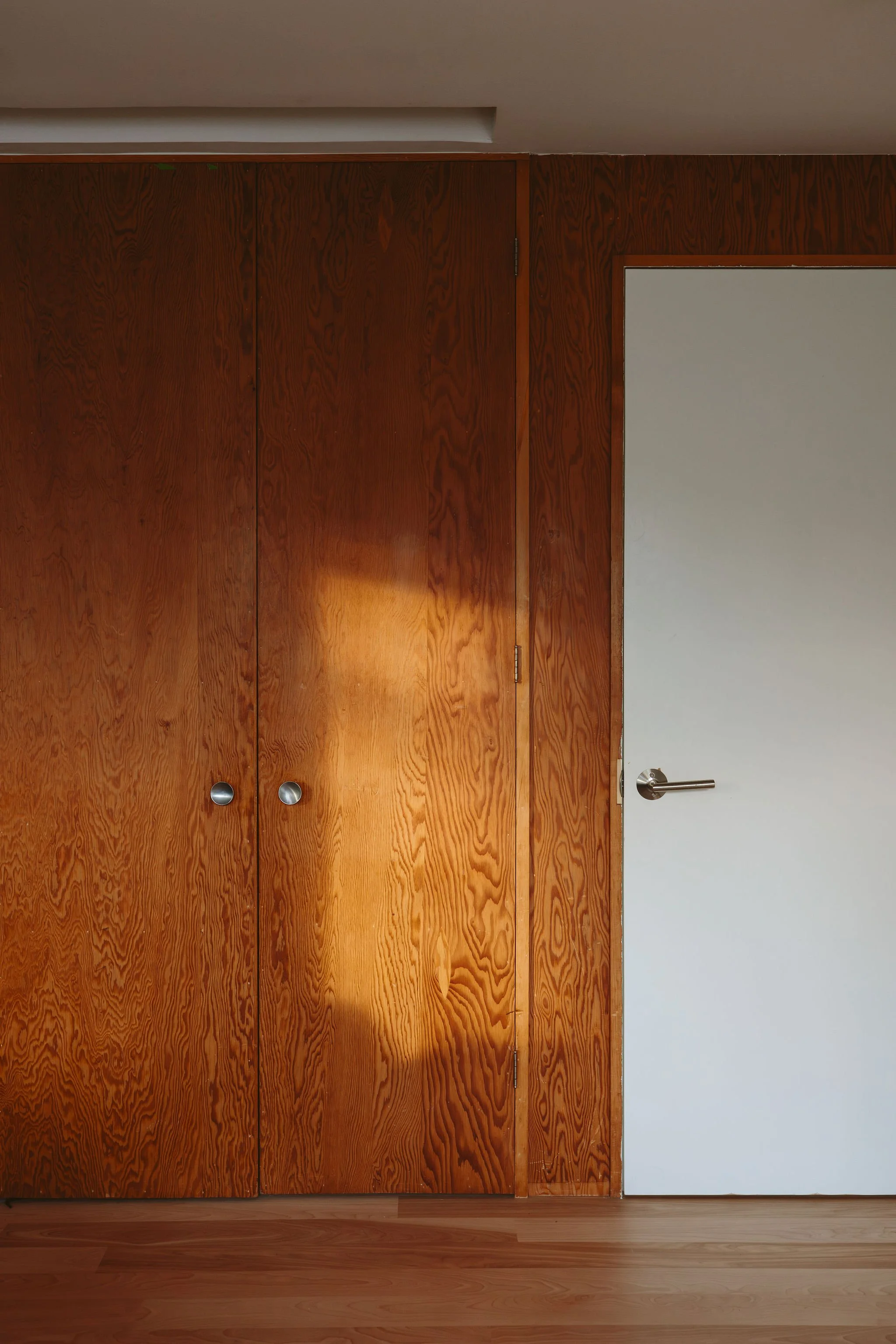 Wooden closet doors and a white door with a silver handle in a room with wooden flooring.