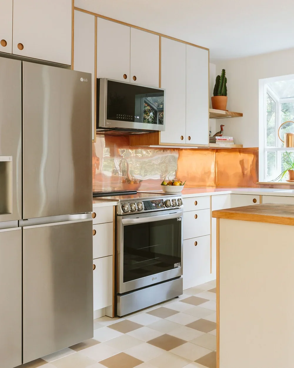 Modern kitchen with white cabinets, stainless steel appliances, a copper backsplash, and a window with potted plants.