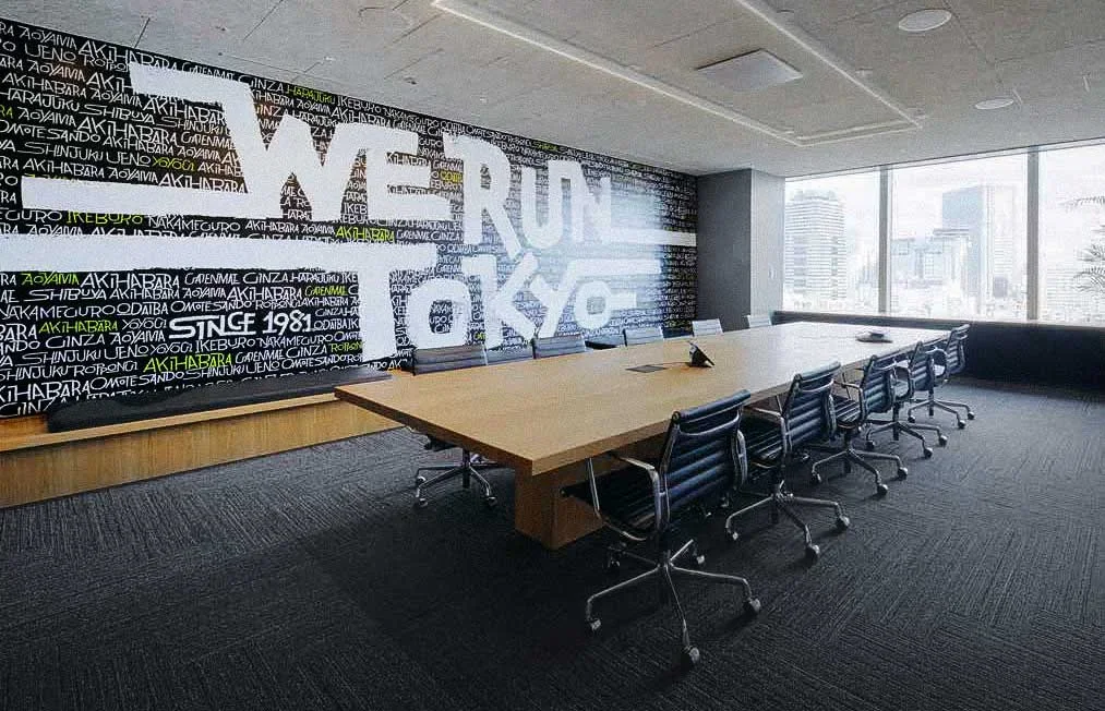 Modern conference room with large wooden table and nine black office chairs, skyline view through large windows, and a black and white wall mural with stylized text.