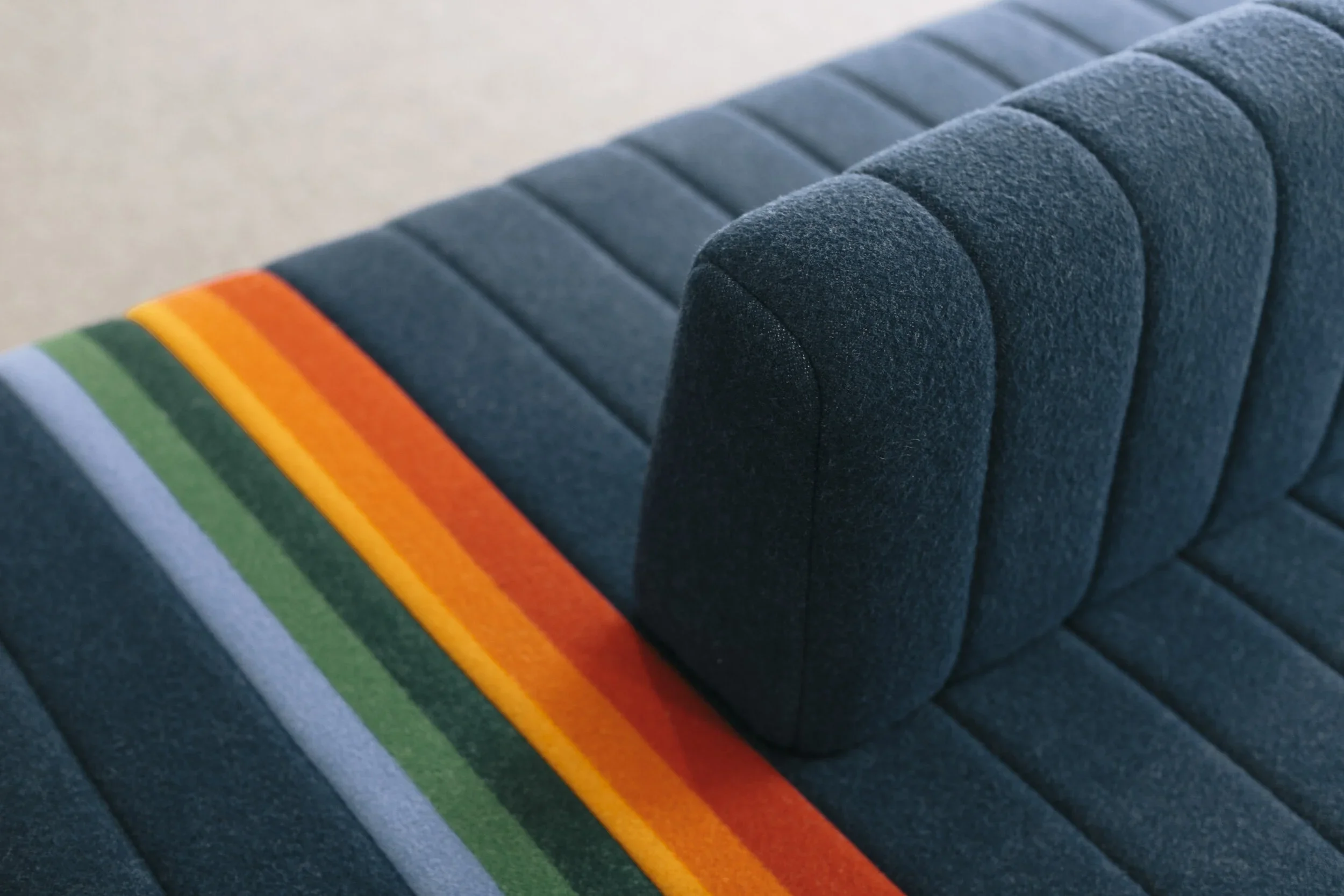 A modern navy blue upholstered sofa with a rainbow-striped blanket on the armrest.