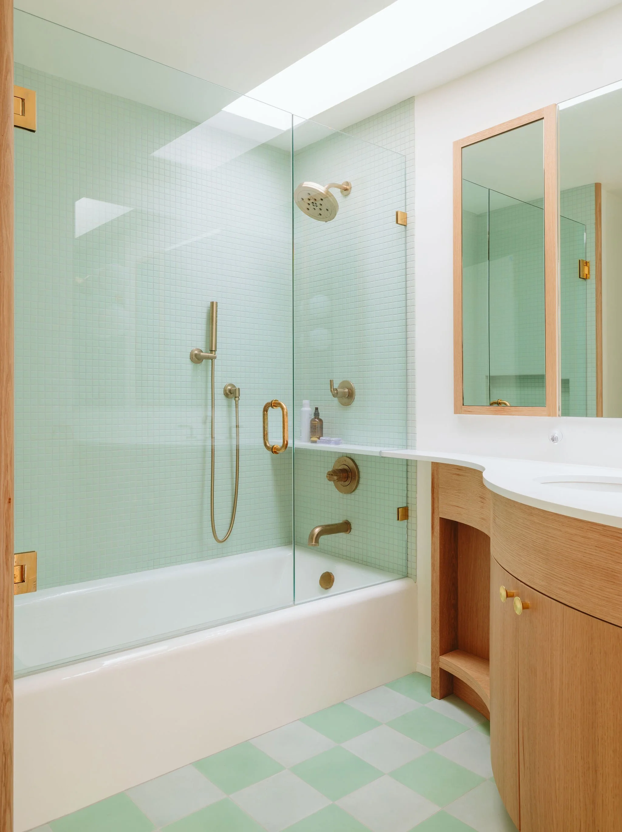 Bathroom with a bathtub, glass shower enclosure, mirror, white sink, and wooden cabinetry, with green and white checkered floor tiles and light green tiled walls.