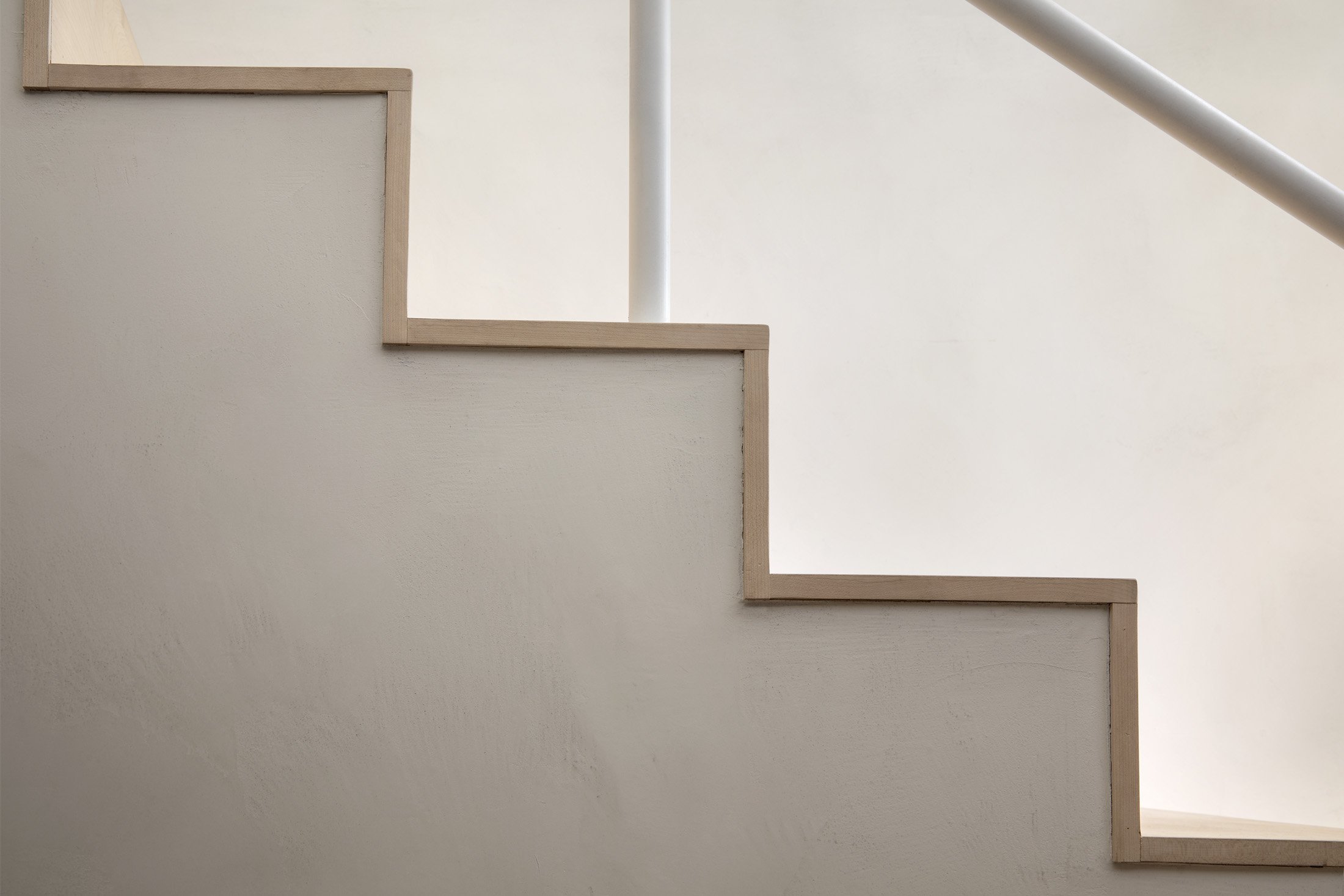Close-up of a staircase with wooden trim and a white handrail against a plain cream wall.