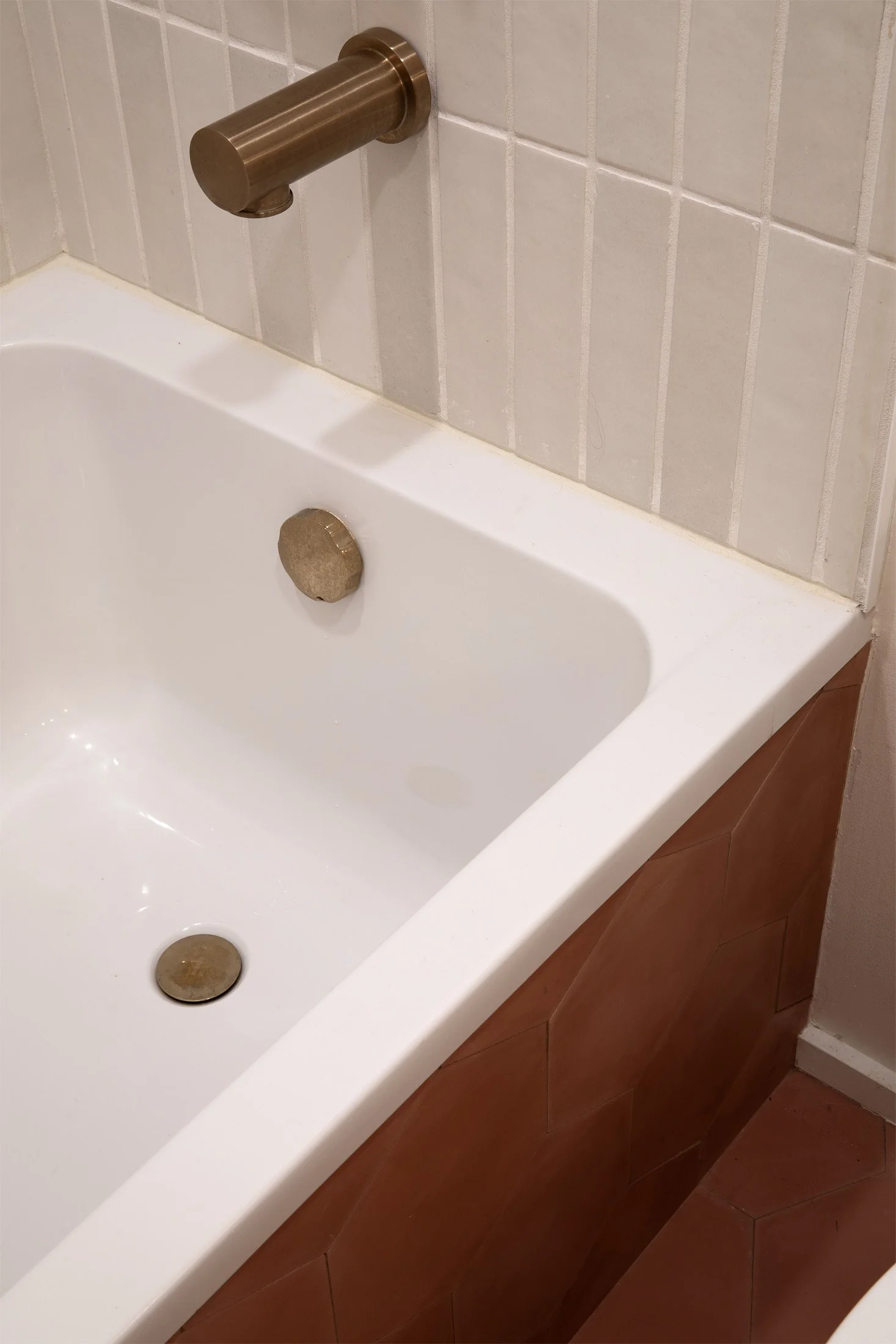 Close-up of a bathtub with a bronze faucet and drain, white interior, beige tiled wall, and brown tiling around the tub.