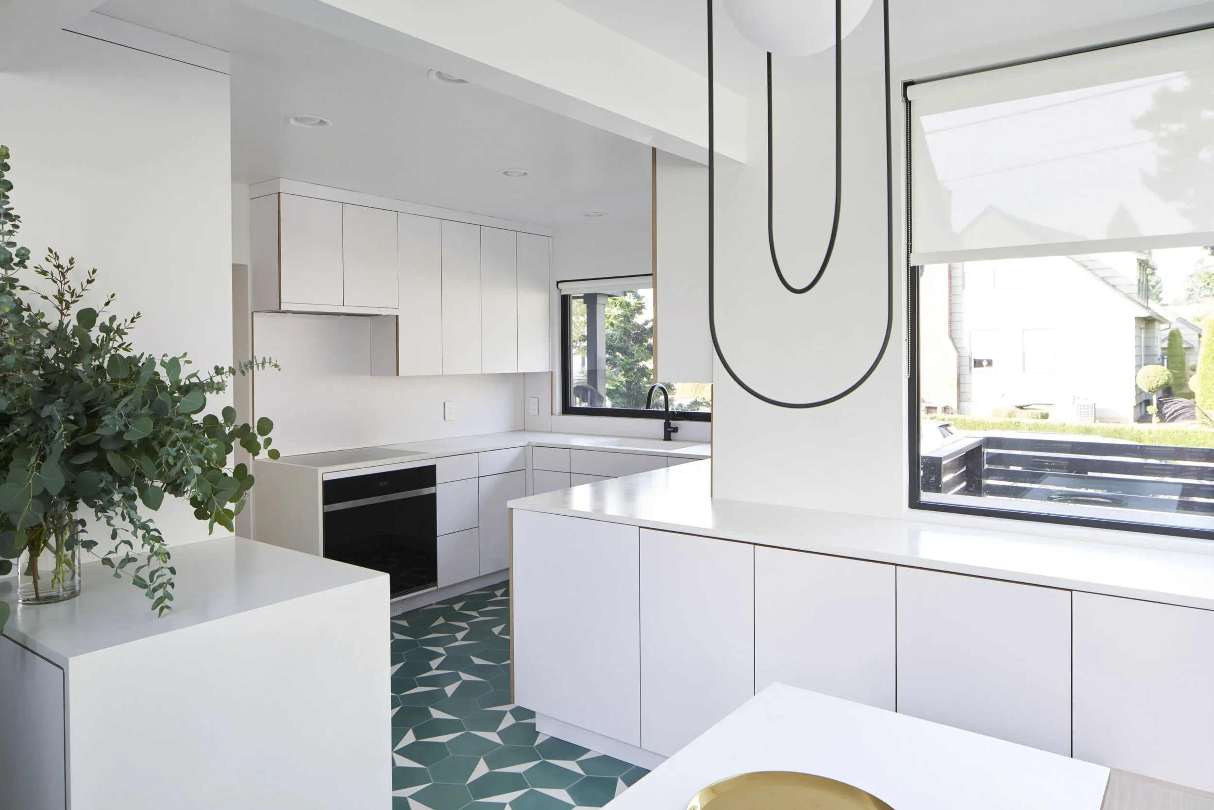 Modern white kitchen with geometric patterned floor, black fixtures, and large window, decorated with a green plant on a white countertop.
