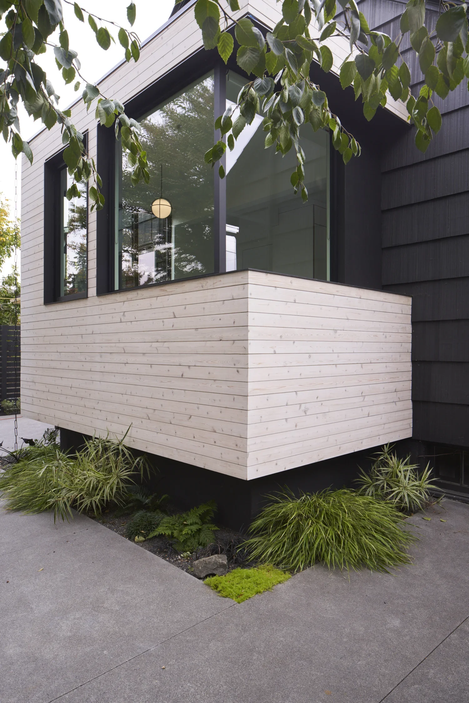 Modern house exterior with a black and white color scheme, large glass window, and a small garden with green plants.