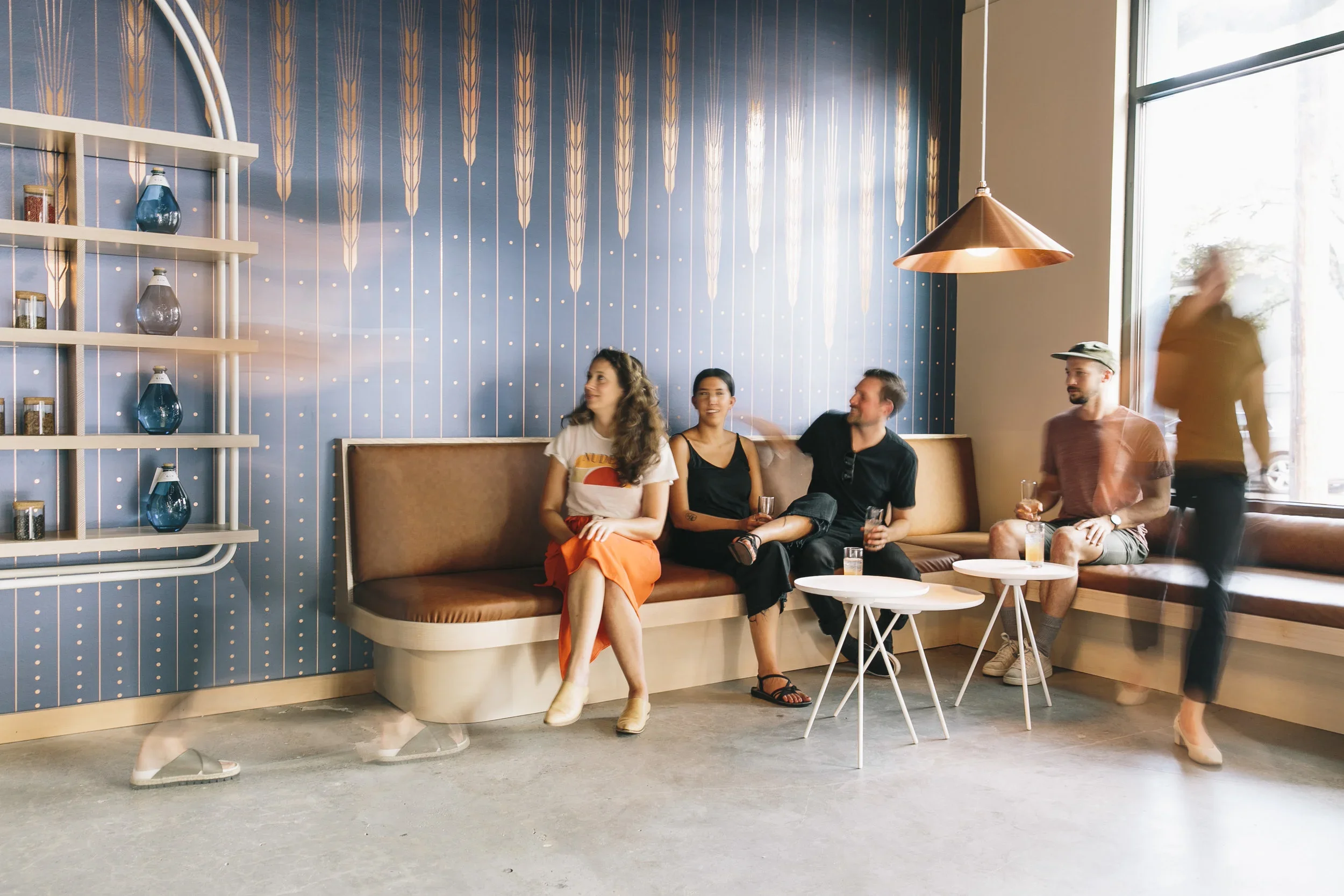 Group of five friends relaxing and chatting in a modern cafe with blue patterned wall and large window.