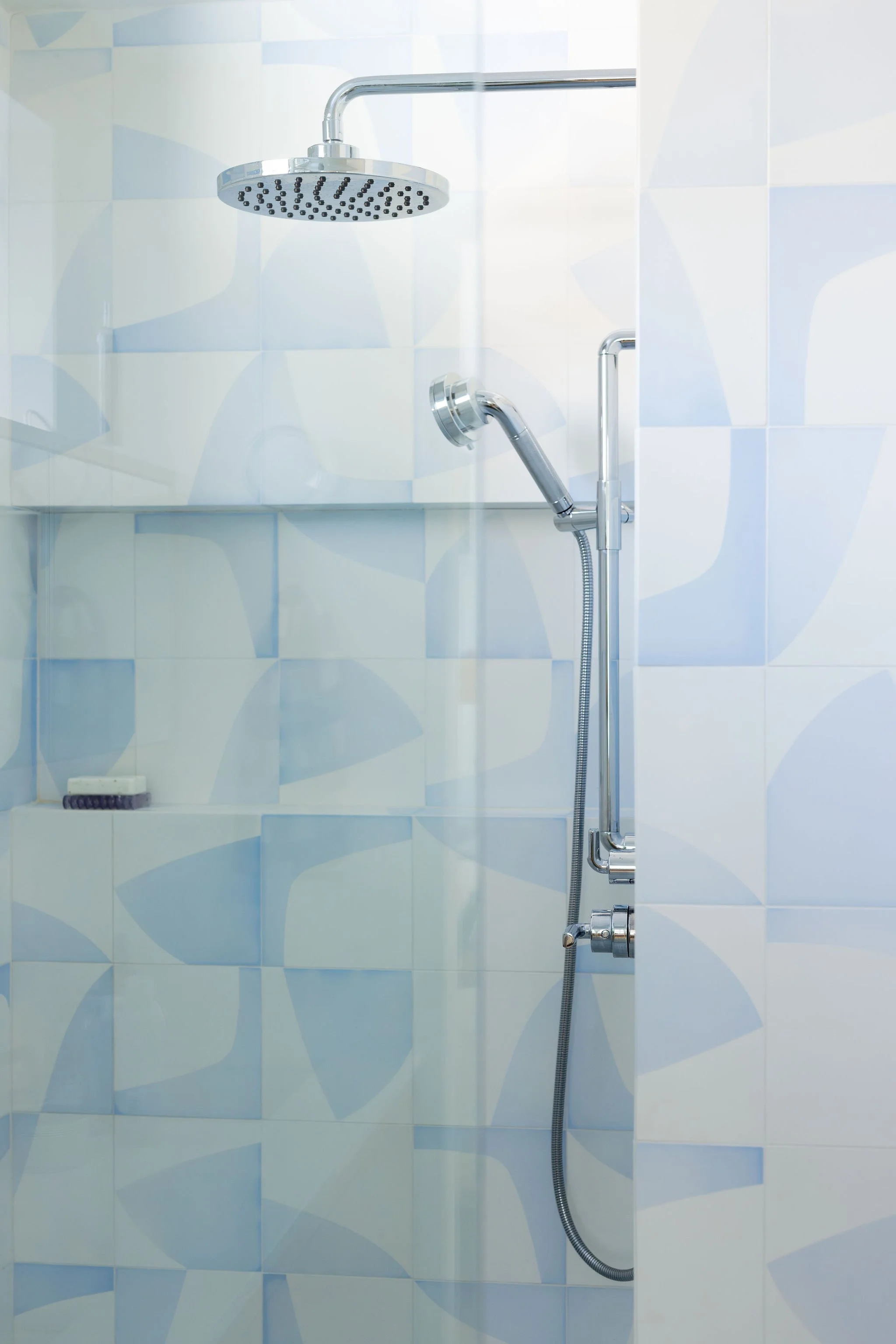 Shower with a chrome rainfall showerhead, handheld spray, and tiled wall with a geometric pattern.