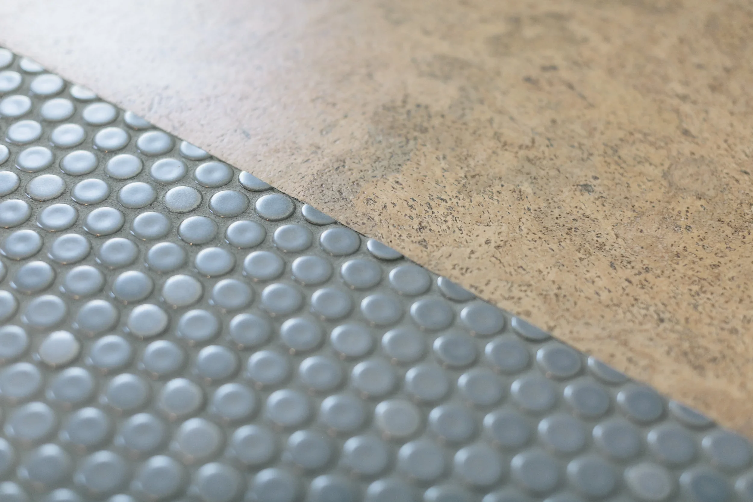 Close-up of a tactile paving surface with raised circular bumps next to a rough textured tile floor.