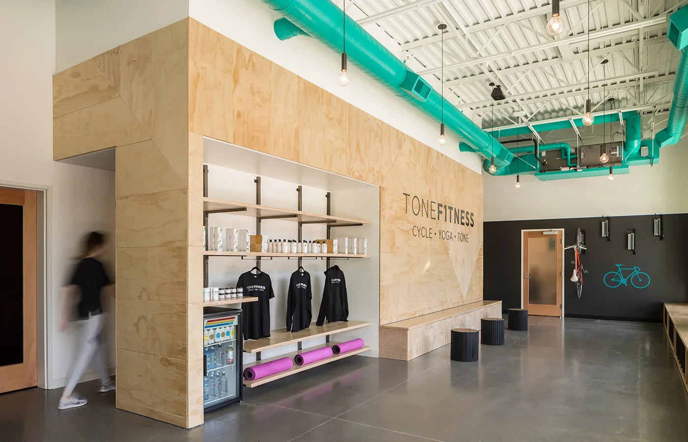 Interior of a fitness studio with wooden and black walls, teal ceiling ducts, and fitness merchandise shelves