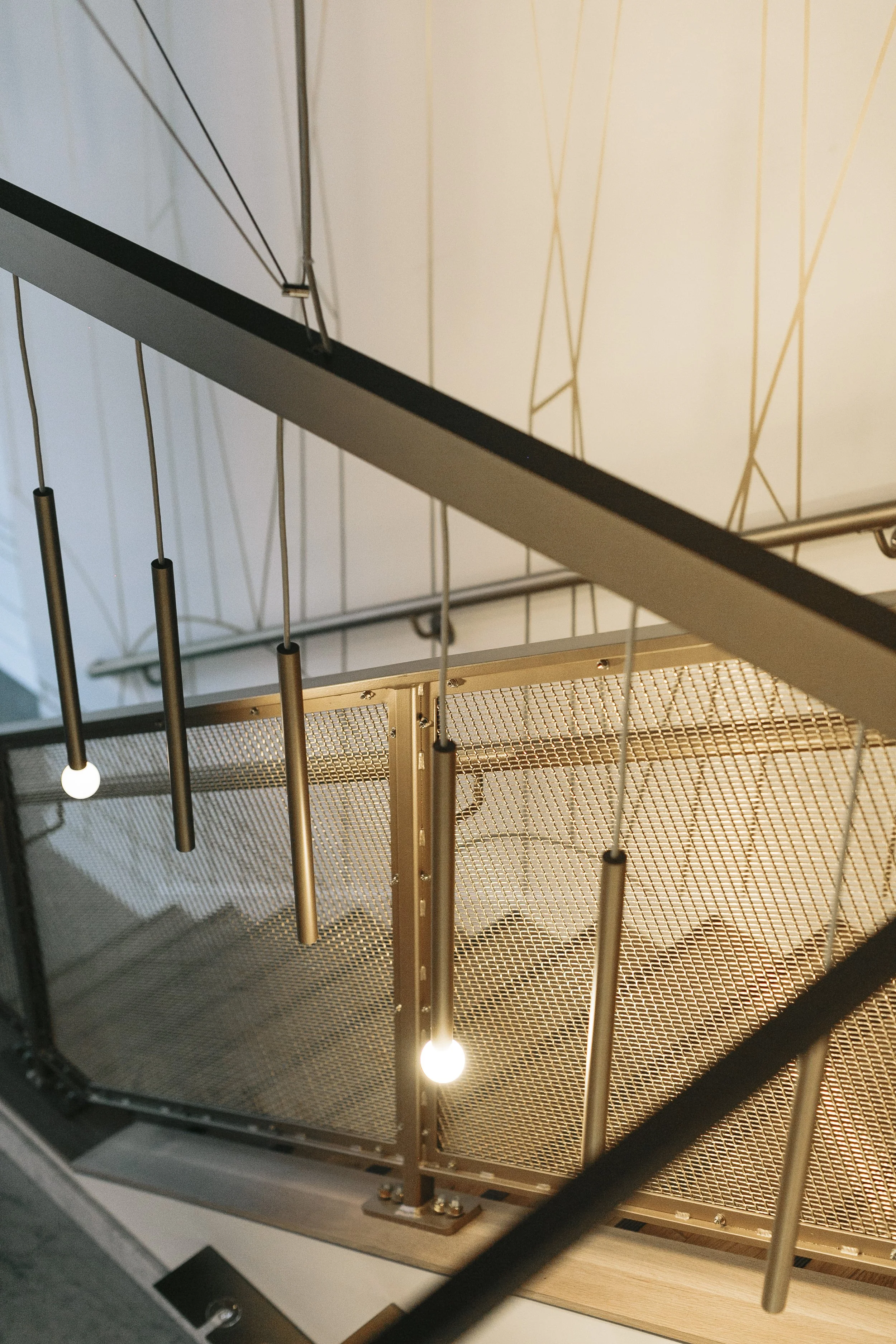 Interior view of modern stairway with metal railings, hanging pendant lights, and a perforated metal floor.