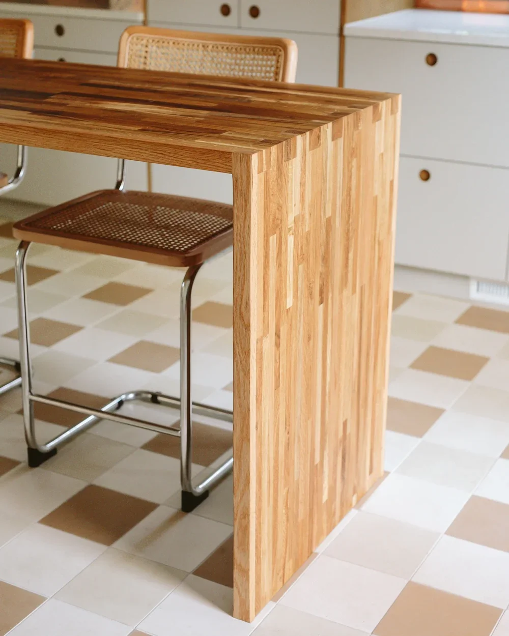 Wooden dining table with a matching chair and tiled floor in a kitchen.