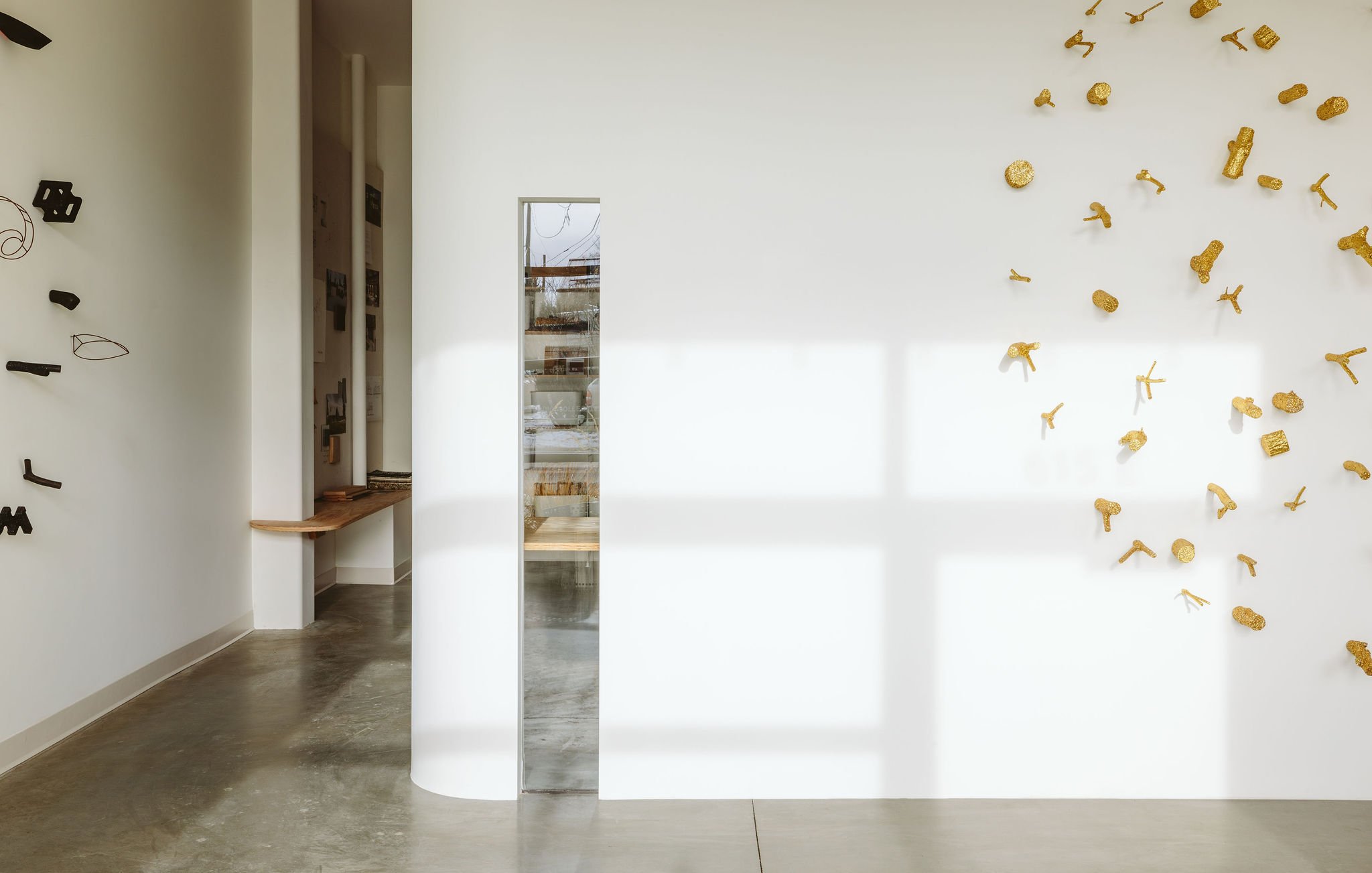 Minimalist art gallery interior with white walls, decorative black and gold art pieces, and a small wooden bench.