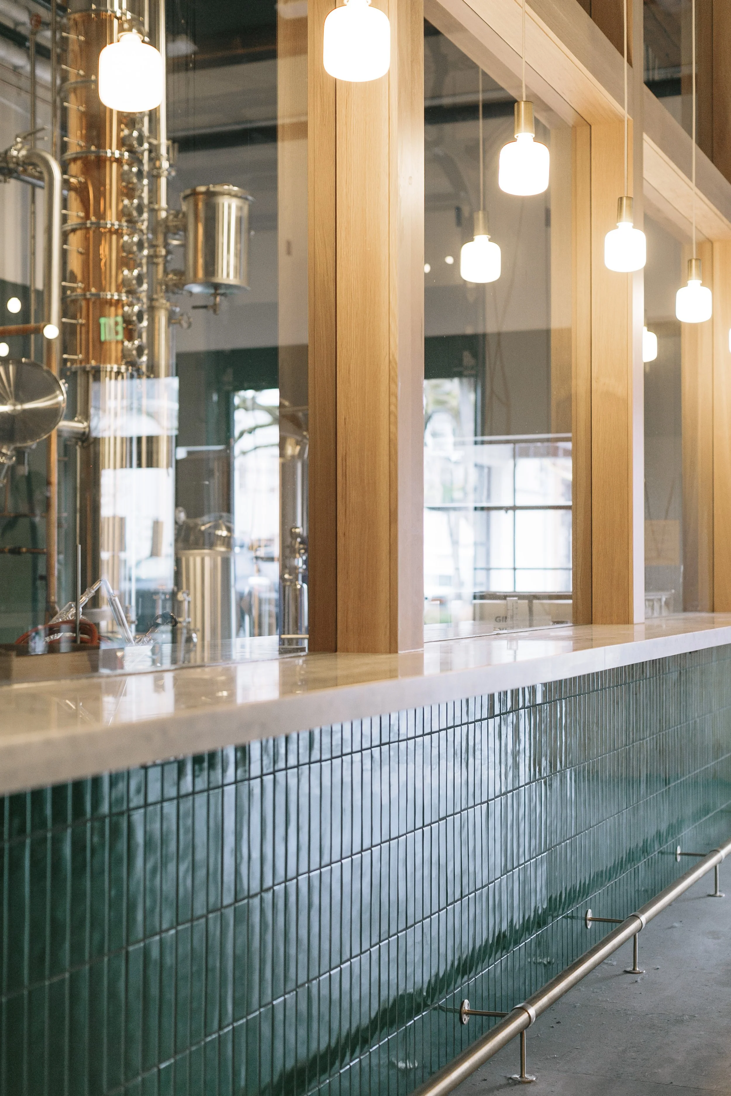 Photo of a bar or restaurant counter with green tile, wooden paneling, glass windows, and warm hanging light fixtures