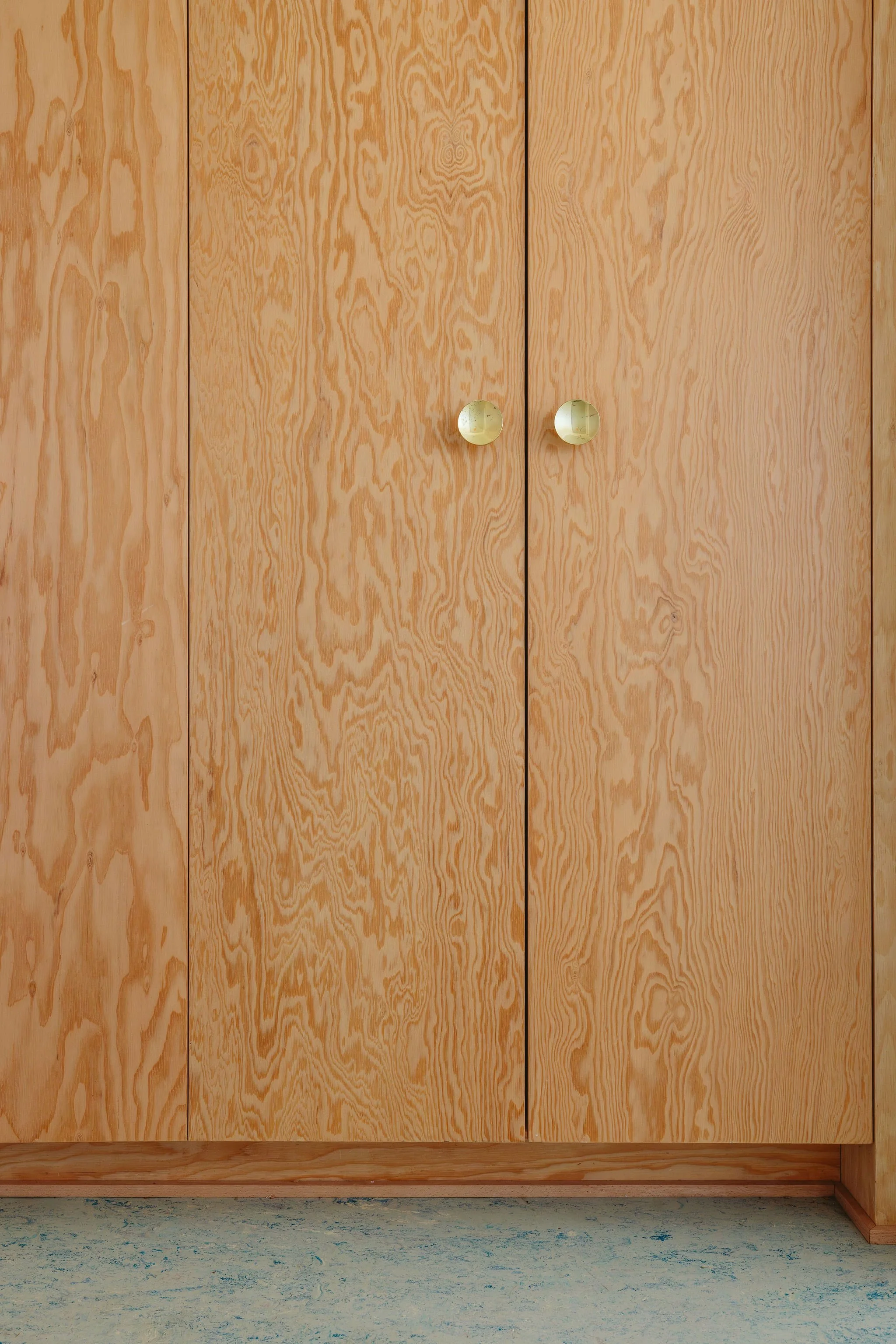 Wooden closet with two doors and round knobs, on a blue and white carpeted floor