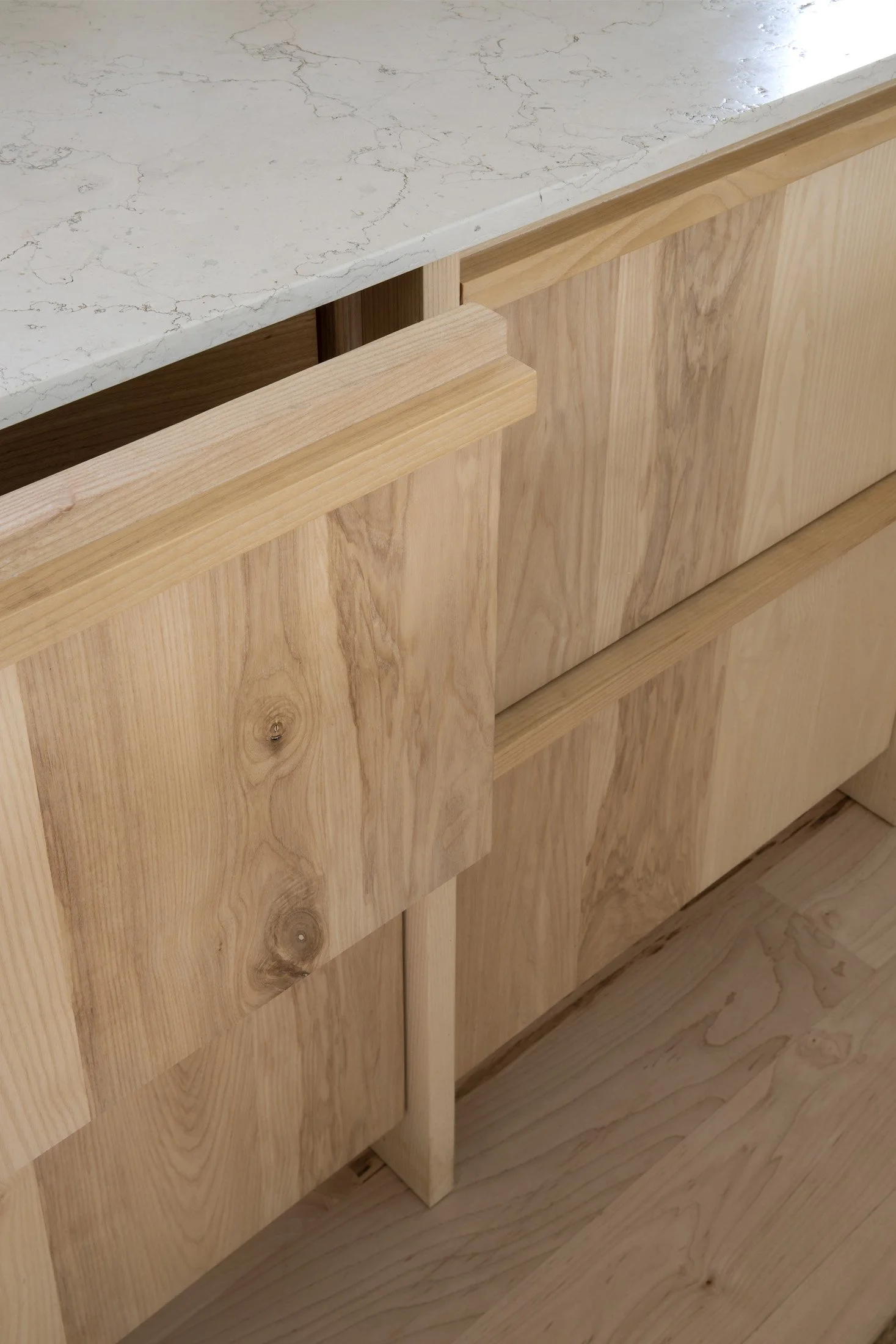 Close-up of a wooden cabinet with a marble countertop, showing the natural wood grain on the cabinet doors and a small wooden support underneath.