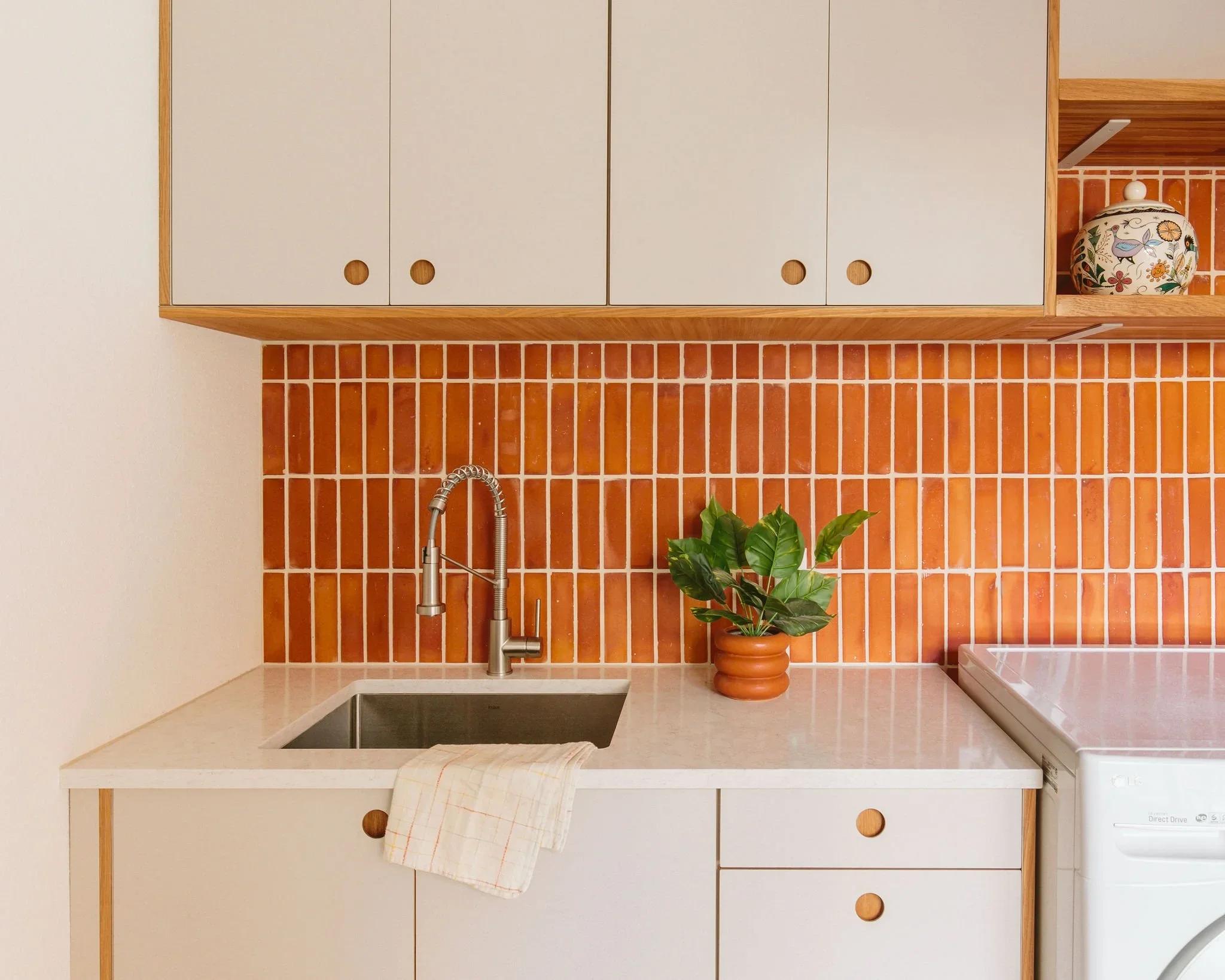Kitchen with white cabinets, orange tile backsplash, stainless steel sink with a faucet, a potted plant, and a washing machine.