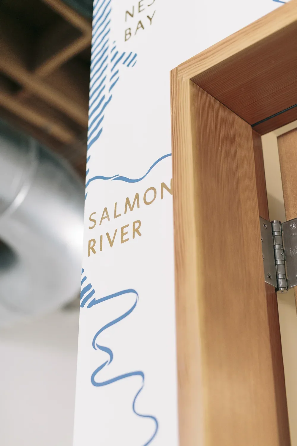 Part of a wall sign with the text 'Salmon River' and some decorative blue line drawings, partially obscured by a wooden door frame.