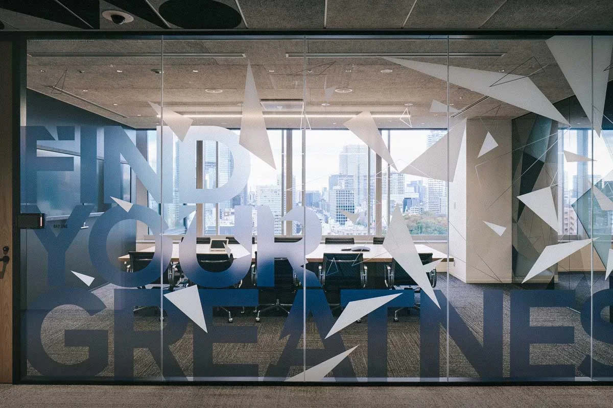 View through a glass conference room wall with a motivational quote and geometric design, overlooking a city skyline.